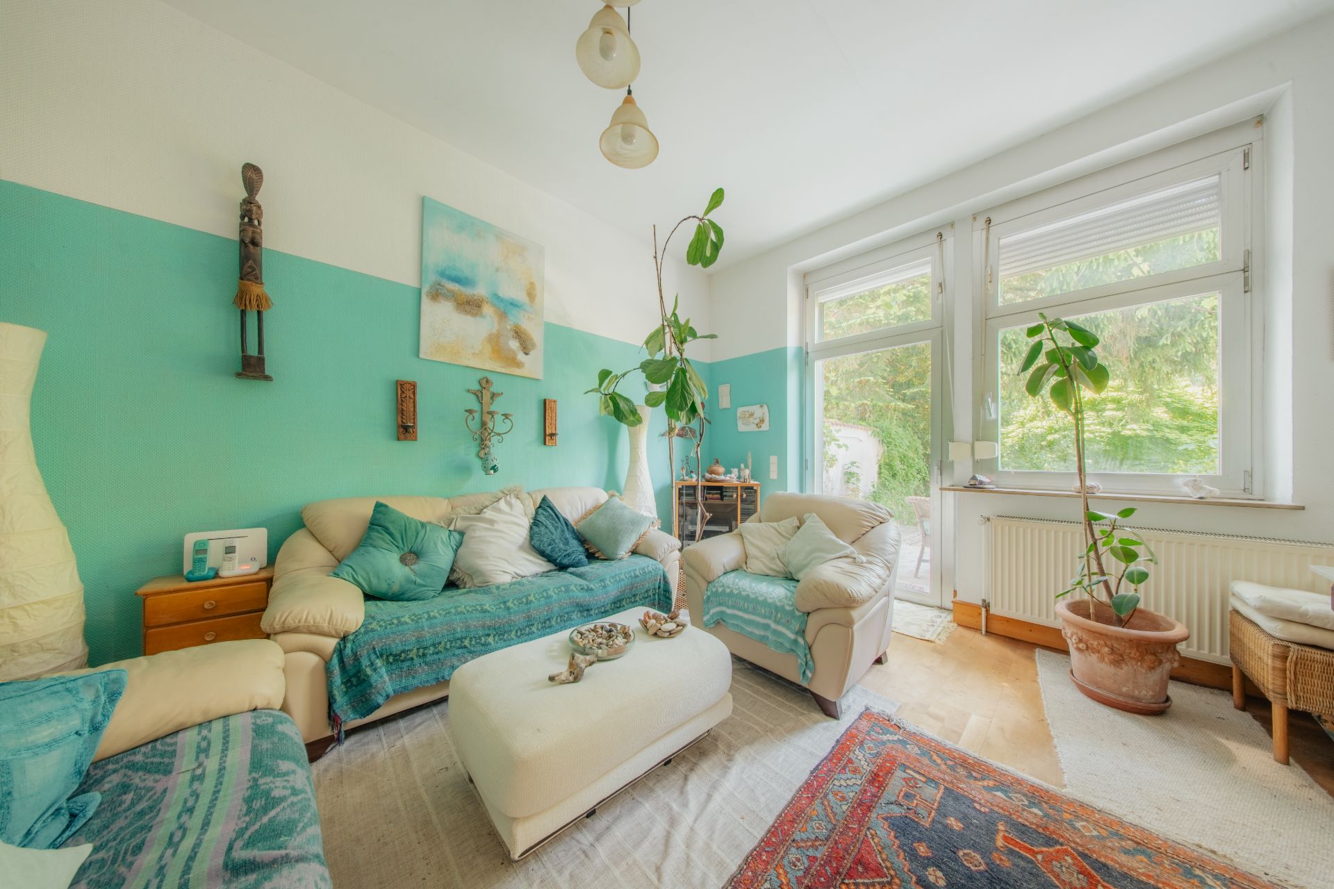 Helles Wohnzimmer mit Sofas, Pflanzen, Couchtisch und großen Fenstern mit Blick ins Grüne.