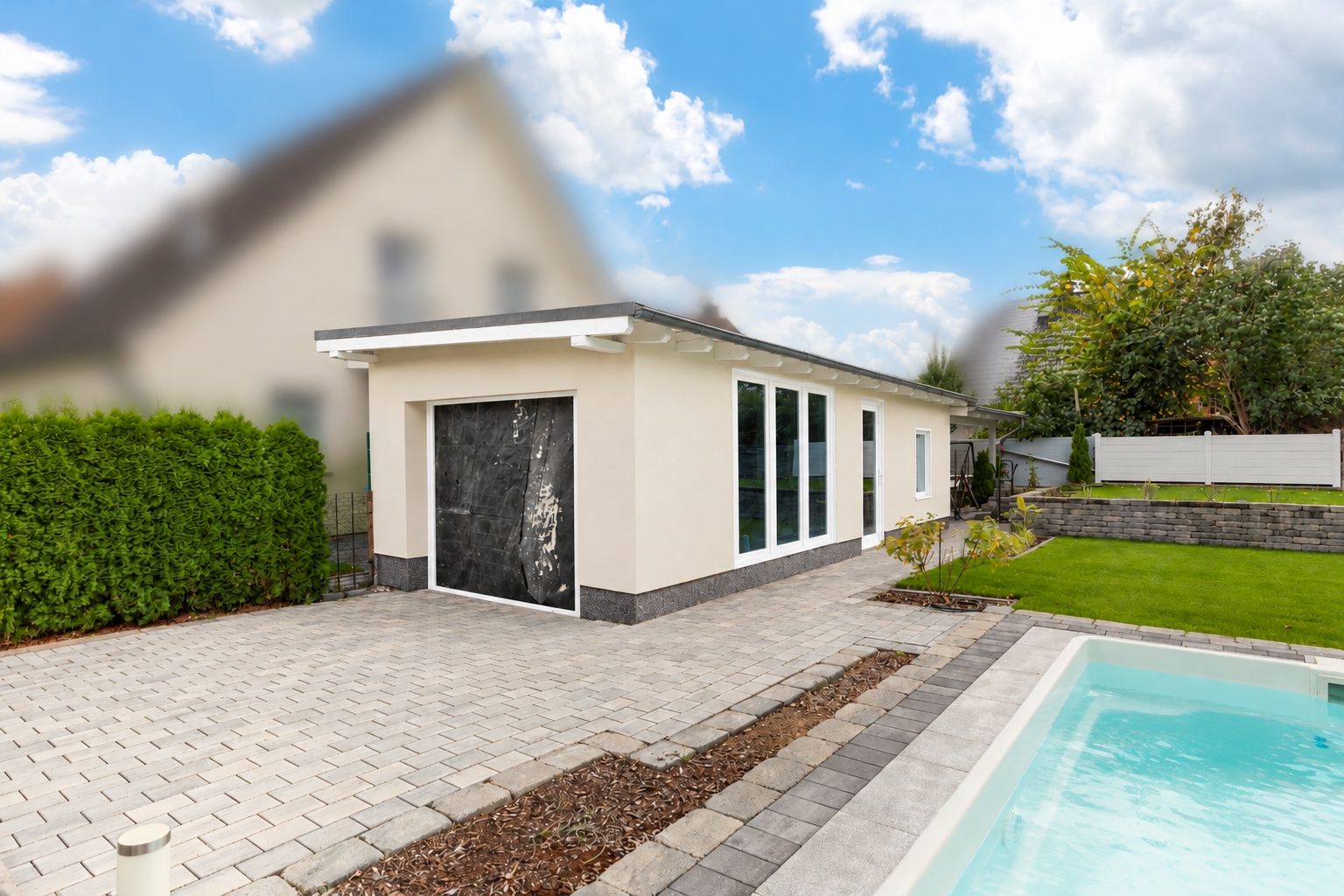 Moderne Garage mit großen Fenstern neben gepflastertem Hof und Pool im Garten.
