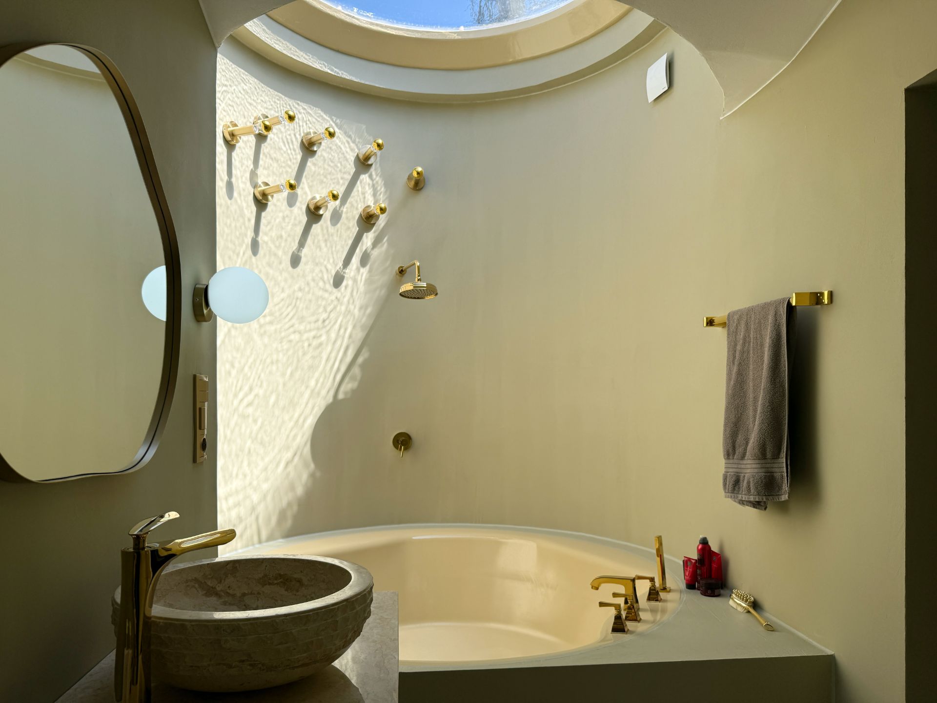 Modernes Badezimmer mit runder Badewanne, Oberlicht, Waschbecken und goldenen Armaturen.