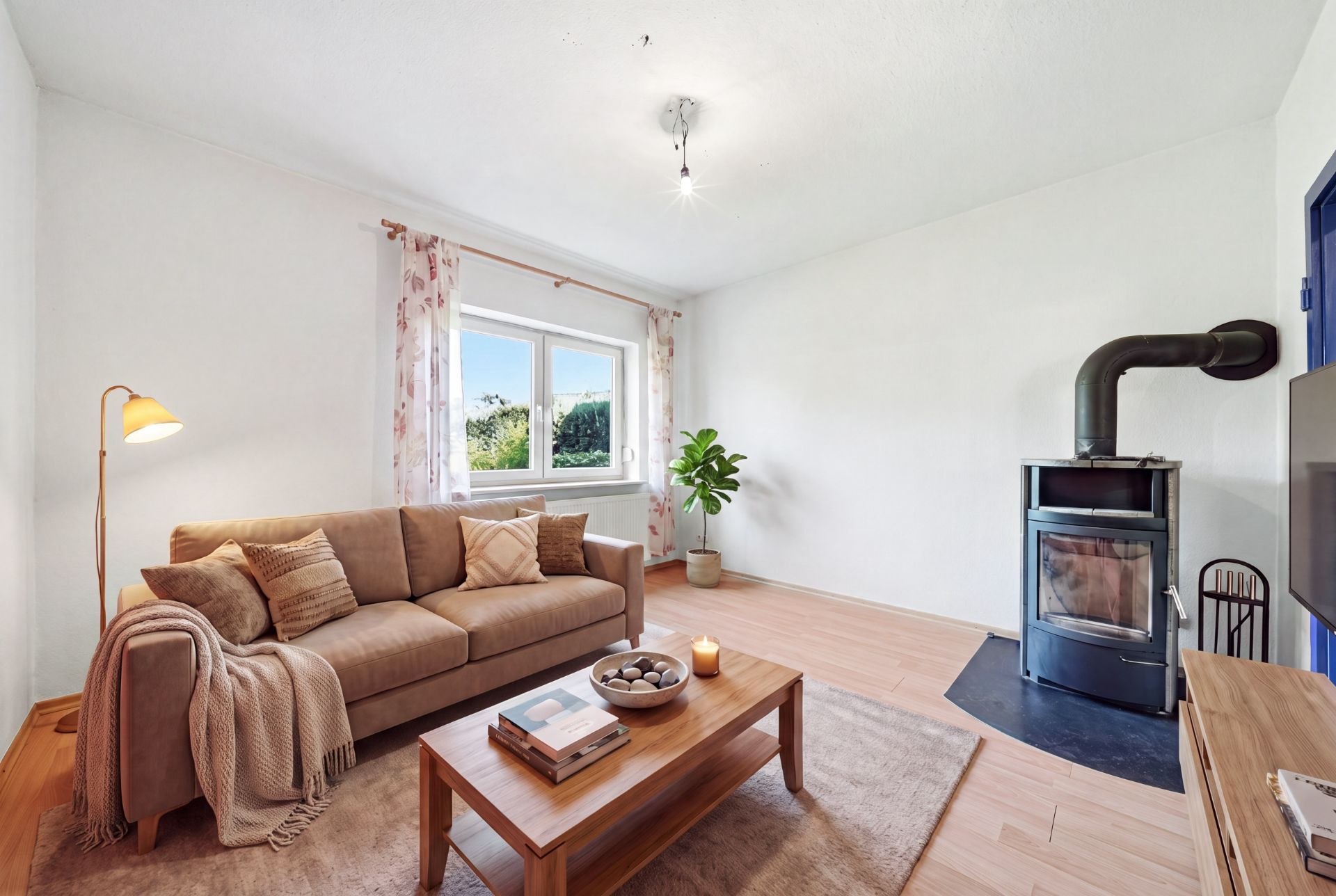 Helles Wohnzimmer mit braunem Sofa, Holztisch, Kaminofen und großem Fenster.
