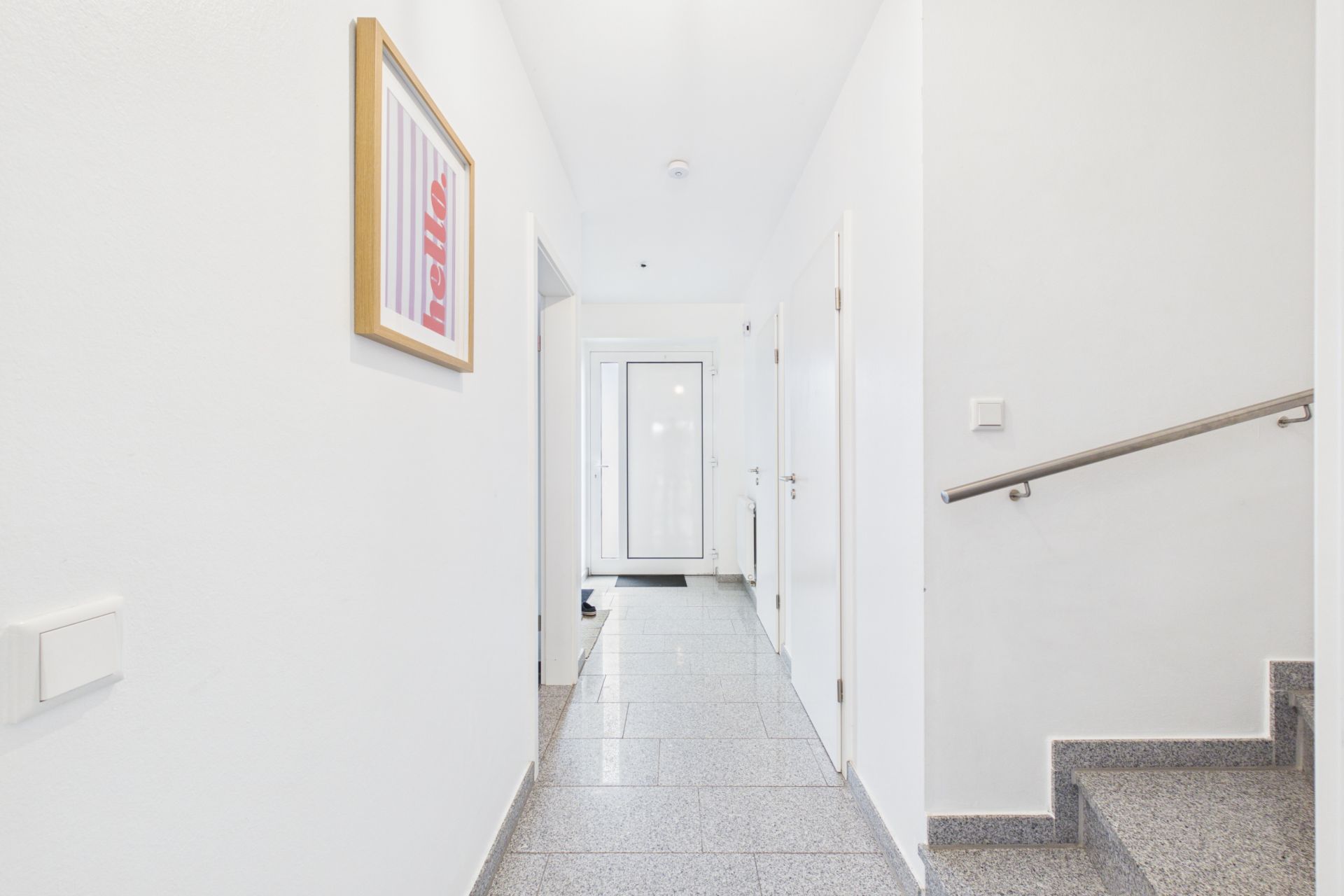 Heller Flur mit Fliesenboden, weißen Wänden, Türen, Treppe und einem gerahmten Bild an der Wand.