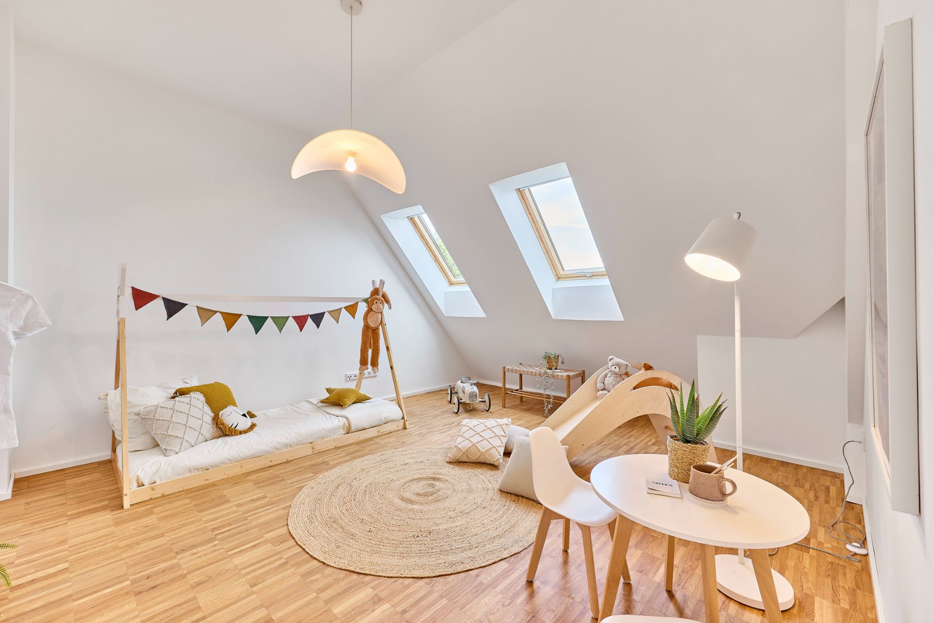 Helles Kinderzimmer mit Bett, Spielzeugpferd, Rutsche, kleinem Tisch und zwei Dachfenstern.