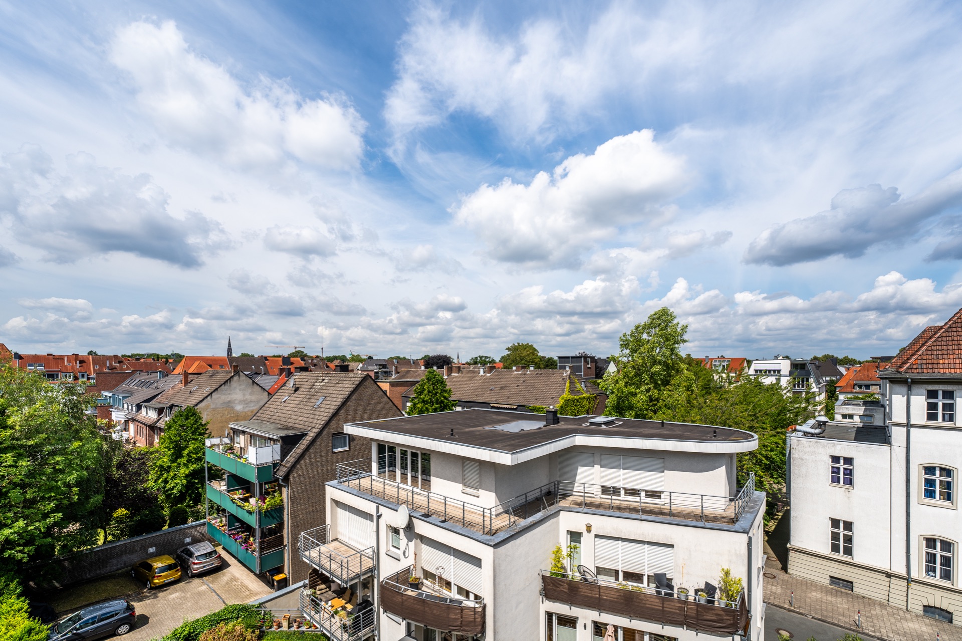Blick auf Wohnhäuser mit Balkonen, Bäumen und teilweise bewölktem Himmel.