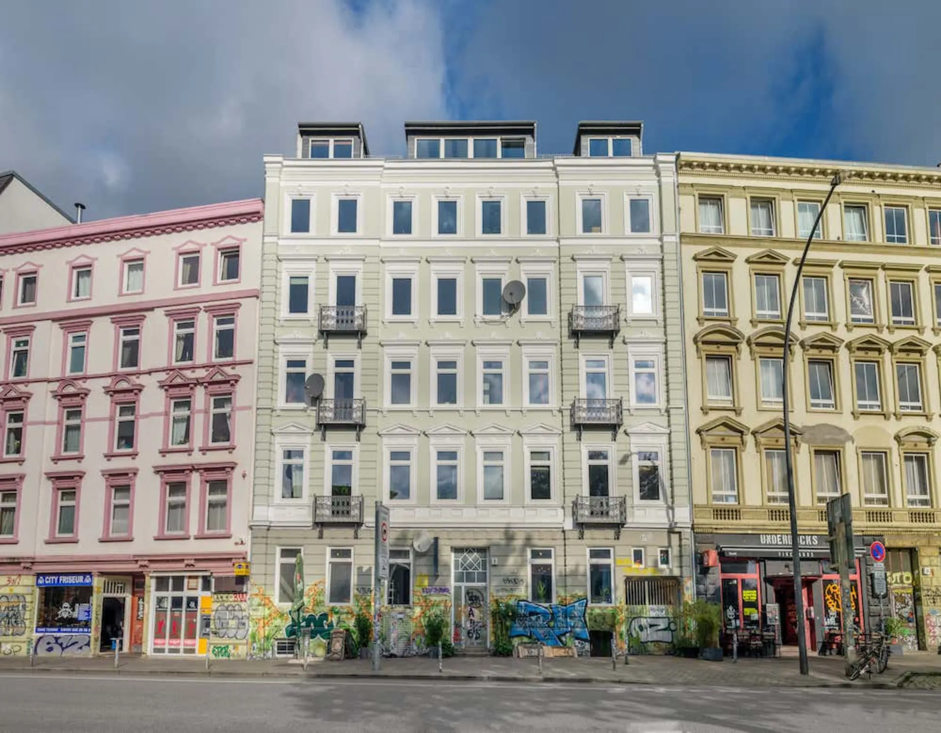 Dreistöckiges Wohnhaus mit Balkonen und Graffiti im Erdgeschoss, umgeben von ähnlichen Gebäuden.