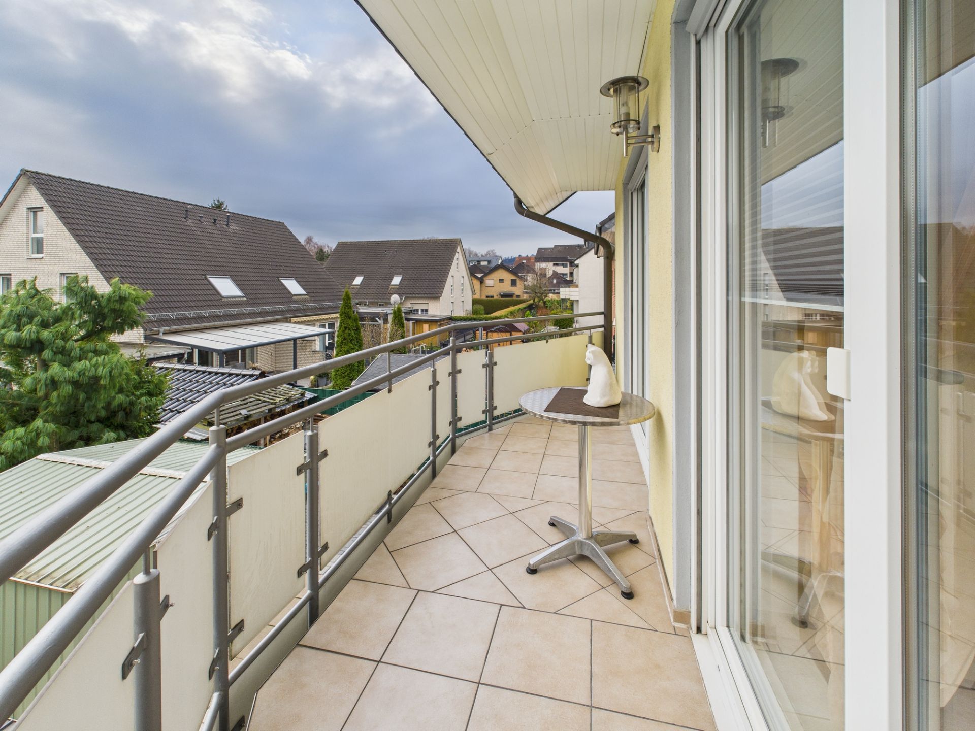 Balkon mit Fliesenboden, rundem Tisch und Blick auf Nachbarhäuser.