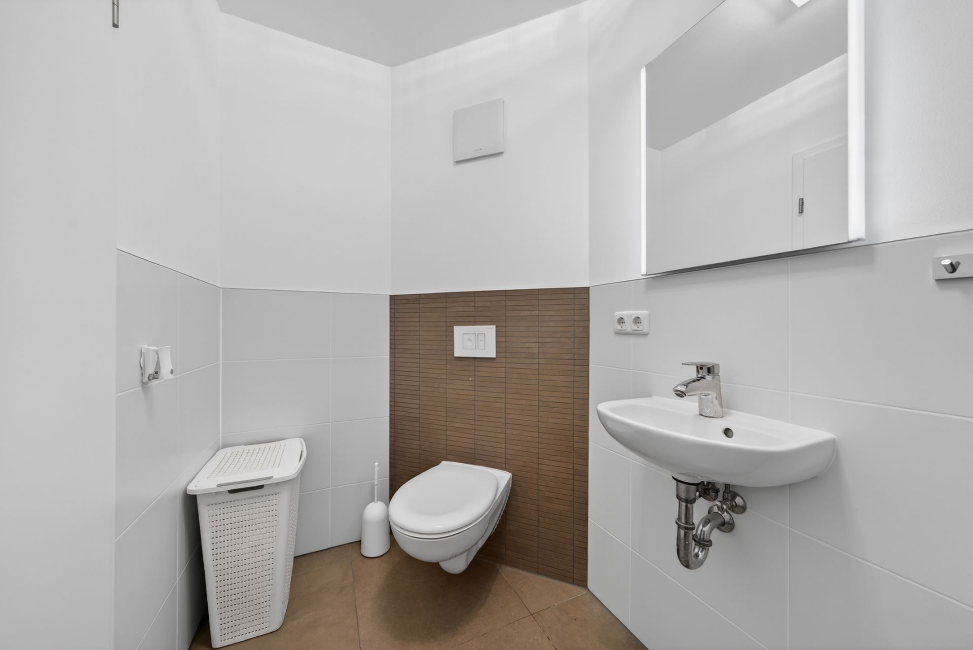 Modernes WC mit wandhängender Toilette, kleinem Waschbecken, Spiegel und Wäschekorb.