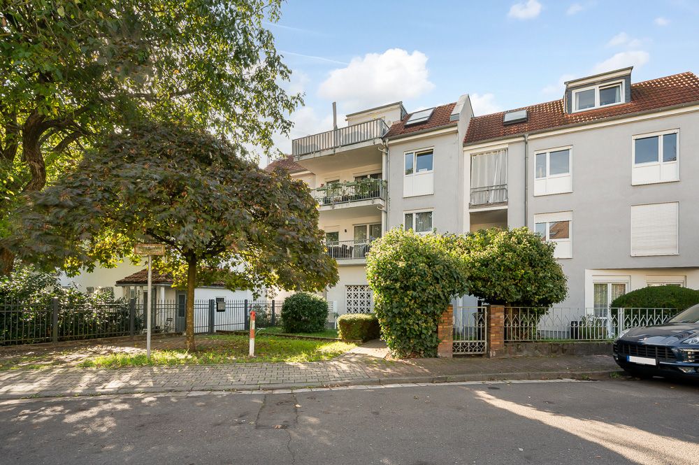 Mehrfamilienhaus mit Balkonen, Bäumen und gepflegtem Vorgarten an einer ruhigen Straße.