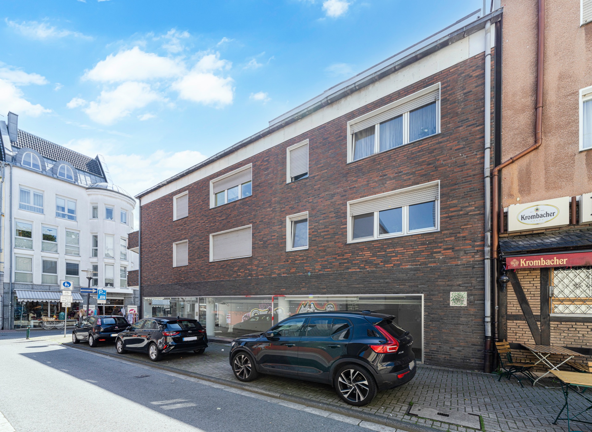 Dreistöckiges Wohnhaus mit dunkelroter Ziegelfassade und geparkten Autos davor.