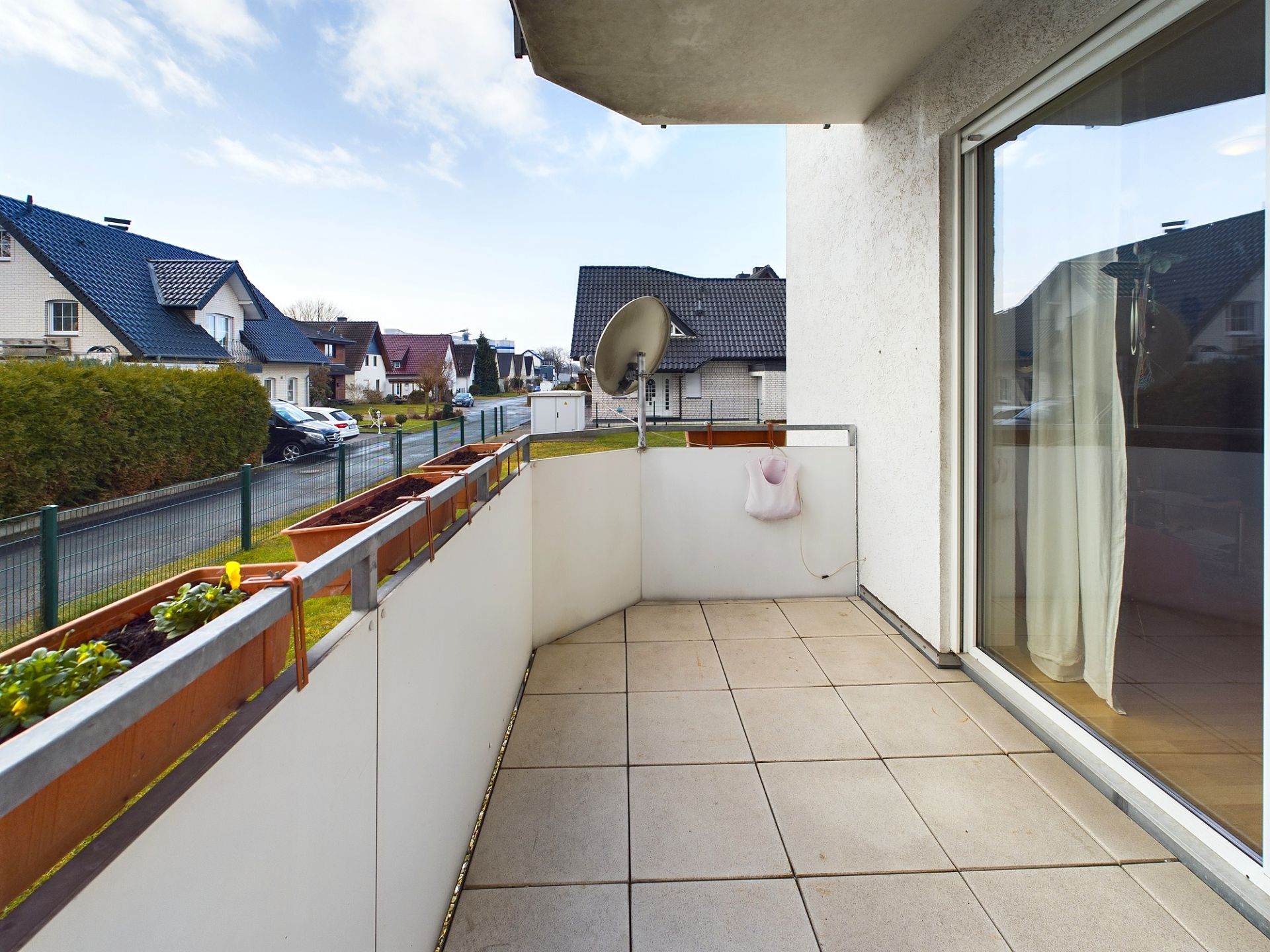 Balkon mit Fliesenboden, Pflanzkästen und Satellitenschüssel in einem Wohngebiet.