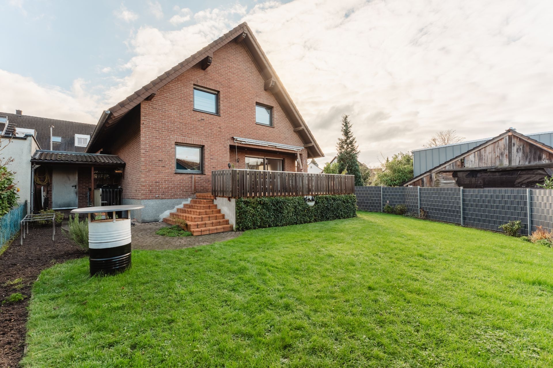 Backstein-Einfamilienhaus mit Terrasse, Treppe und gepflegtem Garten mit Rasenfläche.