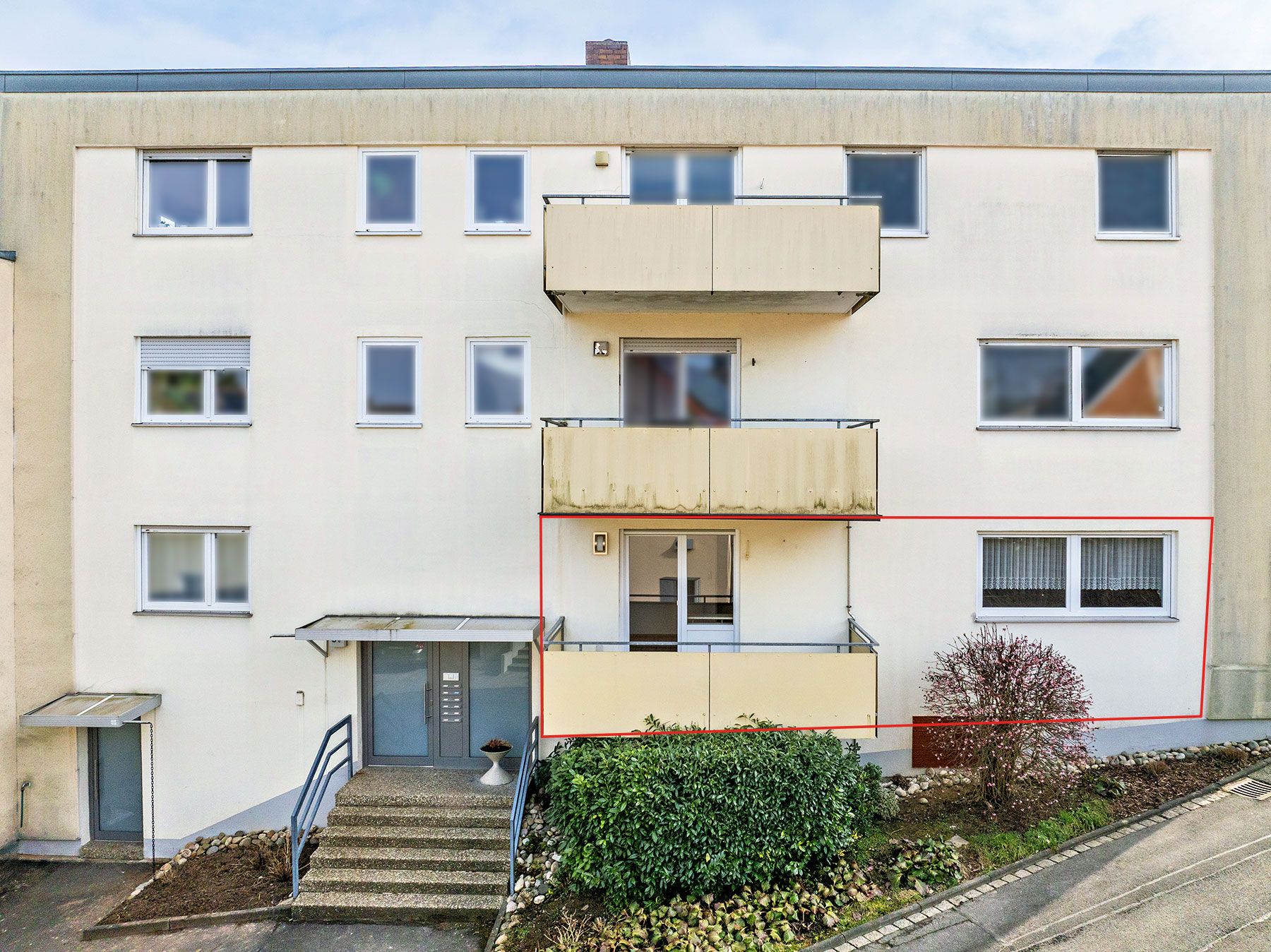 Mehrfamilienhaus mit Balkon und markierter Wohnung im Erdgeschoss.