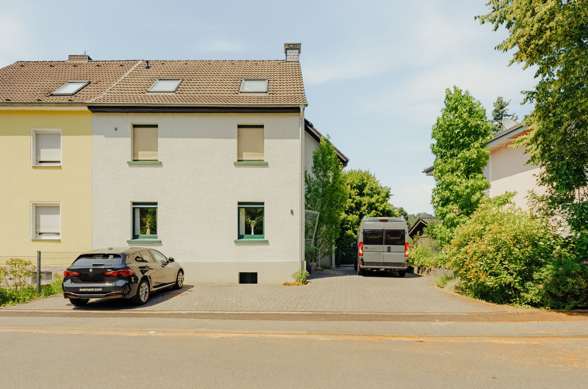 Zweistöckiges Wohnhaus mit zwei geparkten Fahrzeugen auf einer Einfahrt vor dem Haus.