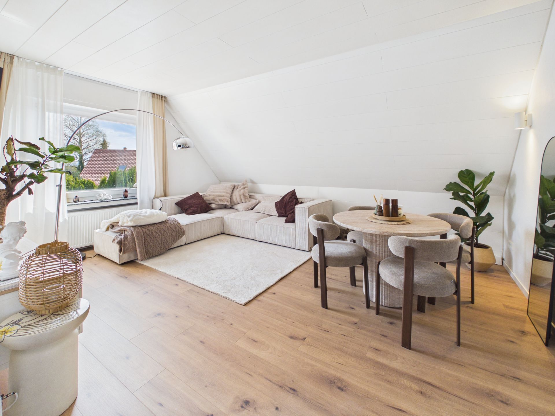 Helles Wohnzimmer mit Ecksofa, rundem Tisch, Teppich und großen Fenstern.