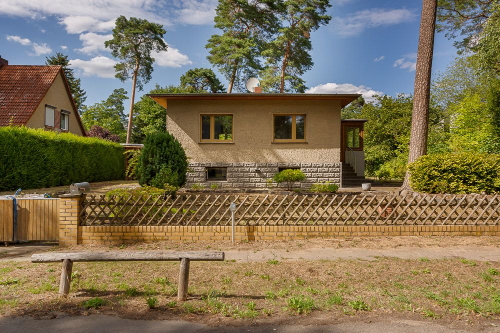 Einfamilienhaus mit Flachdach, Garten und Holzzaun, von Bäumen umgeben.