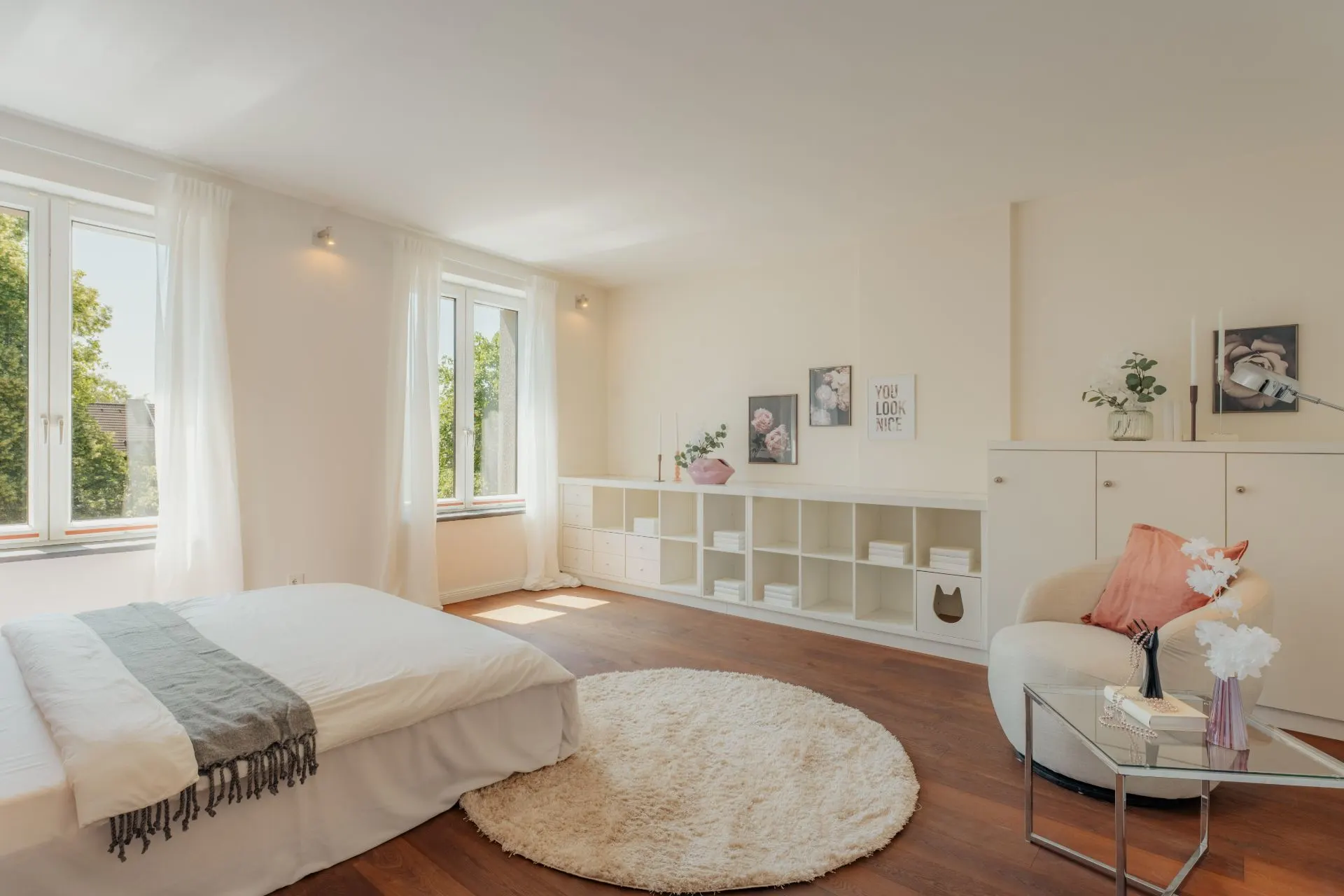 Helles Schlafzimmer mit großem Bett, Sessel, Teppich und Regalen an der Wand.