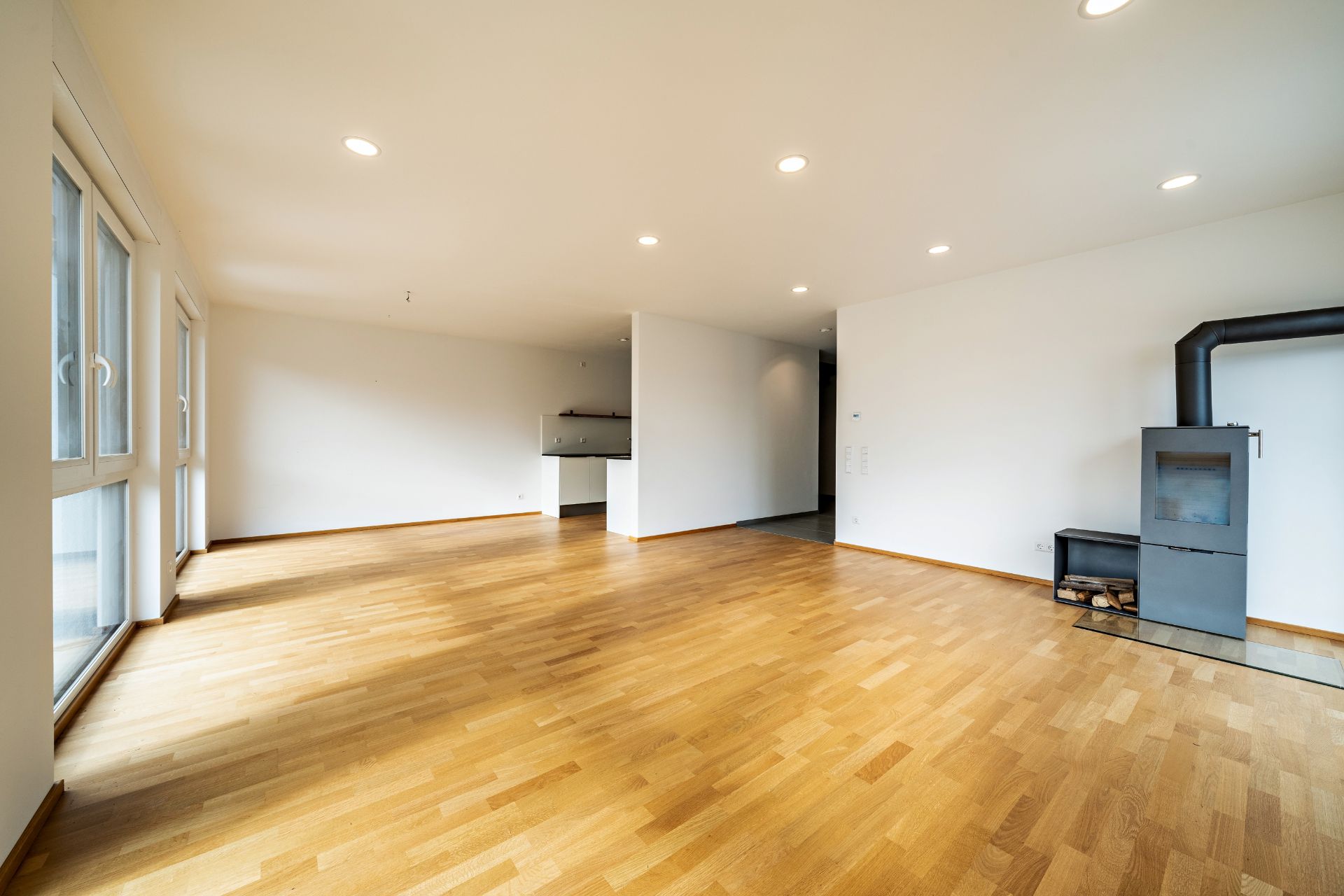 Helles Wohnzimmer mit Holzfußboden, großen Fenstern und Kaminofen.
