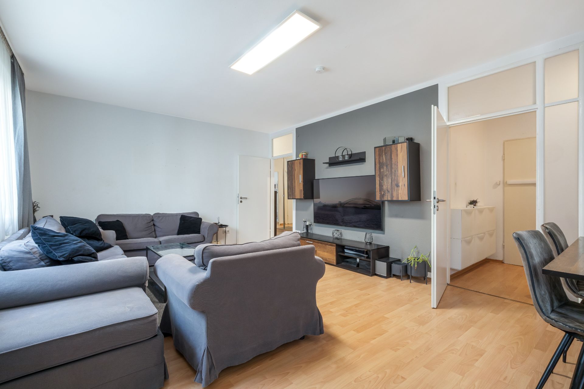 Wohnzimmer mit grauen Sofas, Fernseher an der Wand und Holzboden.