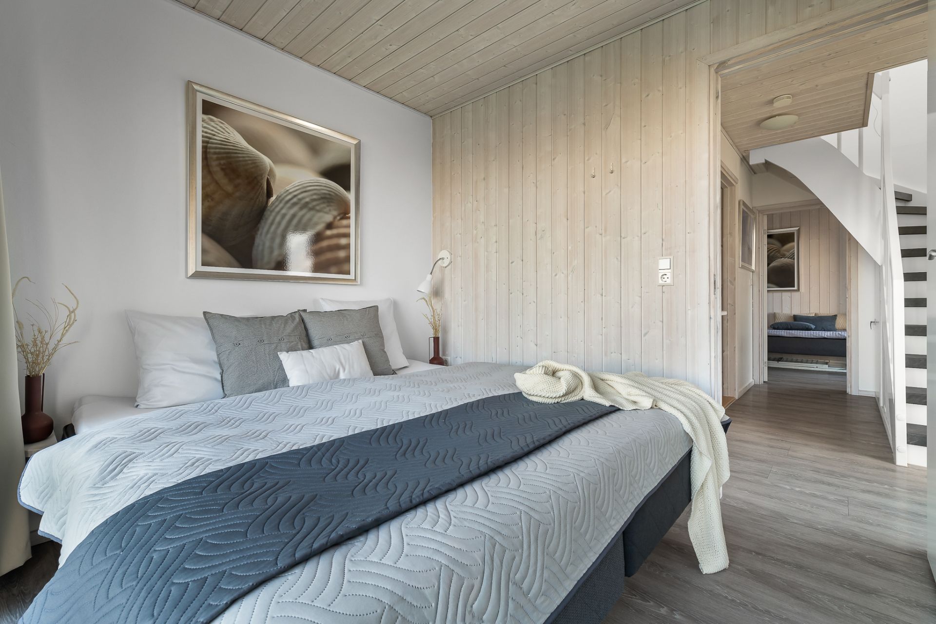 Modernes Schlafzimmer mit Doppelbett, grauen Kissen und Holzdecke, Flur und Treppe im Hintergrund.