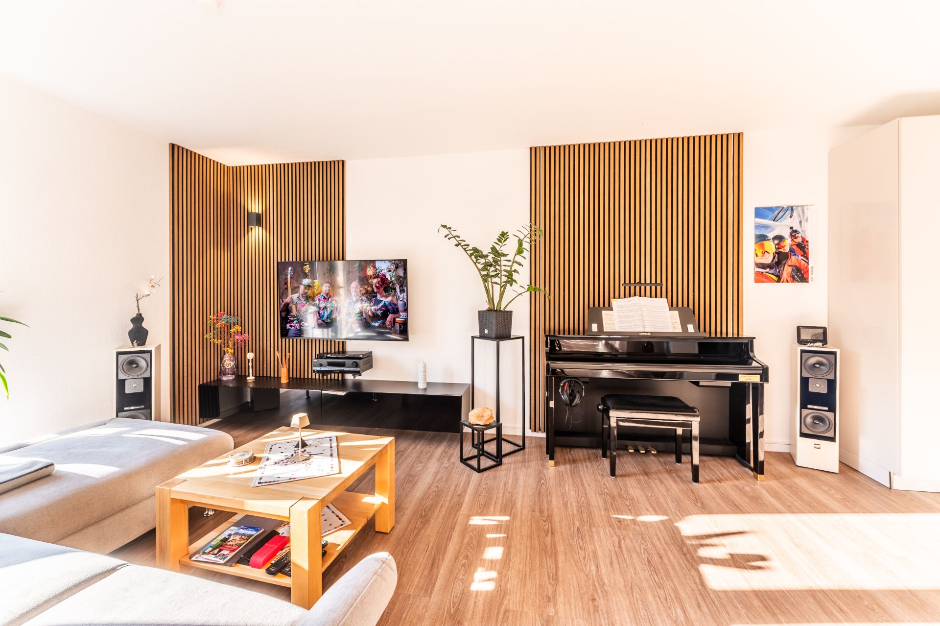 Helles Wohnzimmer mit Sofa, Couchtisch, Fernseher, Klavier und Holzwandpaneelen.