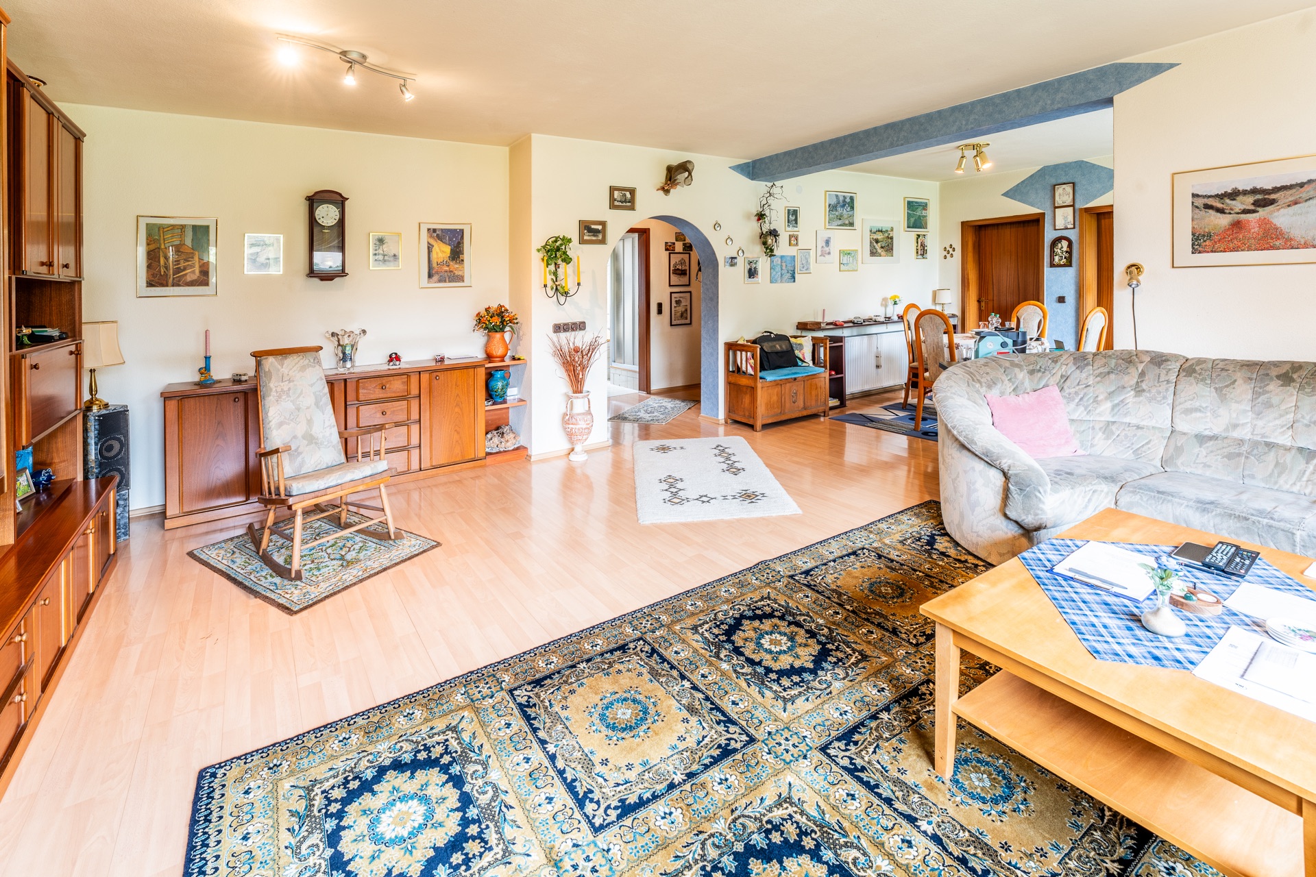 Helles Wohnzimmer mit Teppich, Sofa, Holzmöbeln und vielen Bildern an den Wänden.
