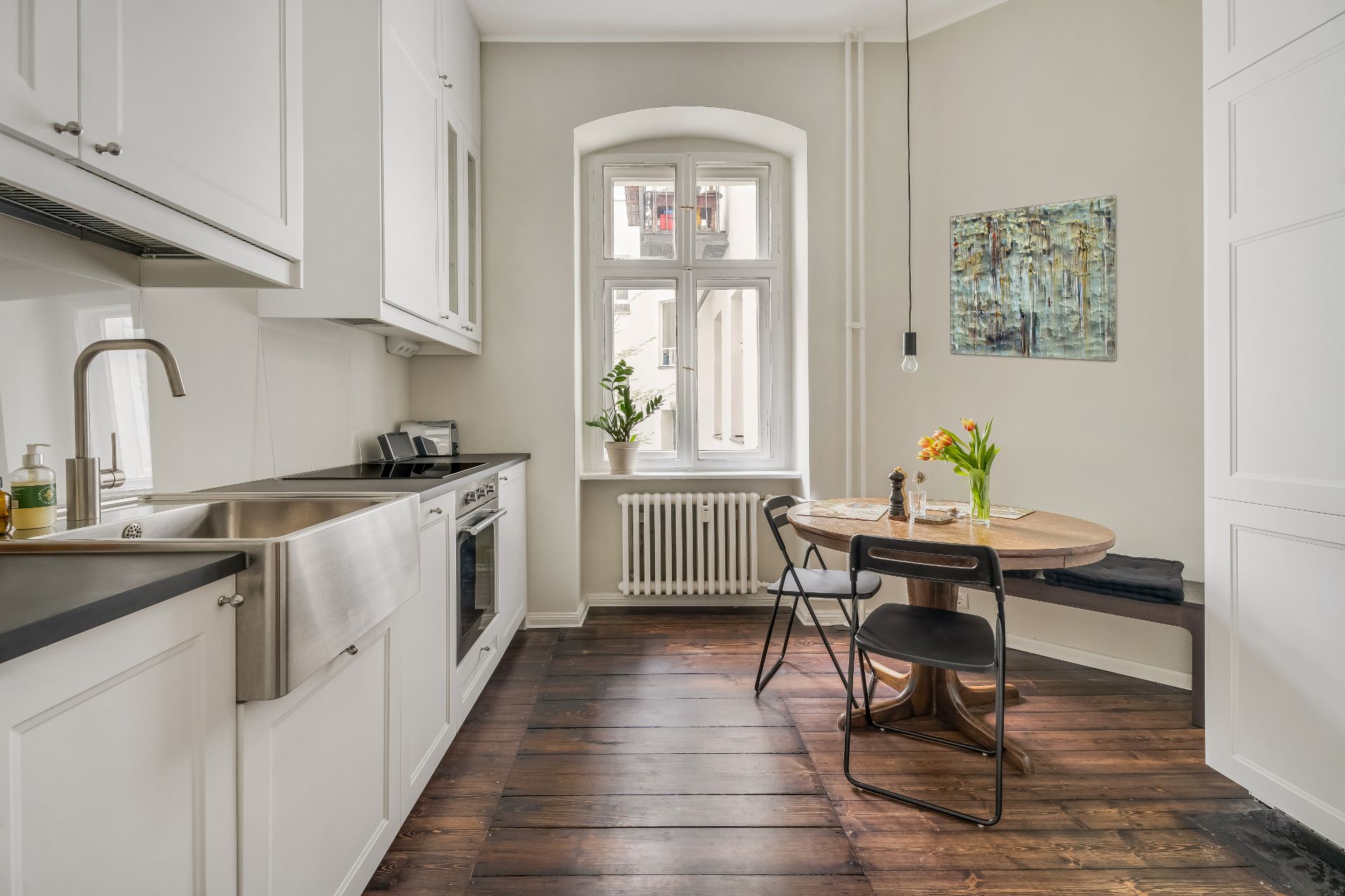 Helle Küche mit Holzboden, Esstisch, zwei Stühlen und Fenster mit Pflanzen.