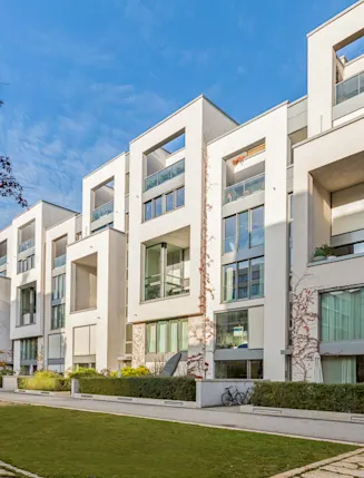 Moderne Wohngebäude mit großen Fenstern und Balkonen, davor ein gepflegter Gartenweg.
