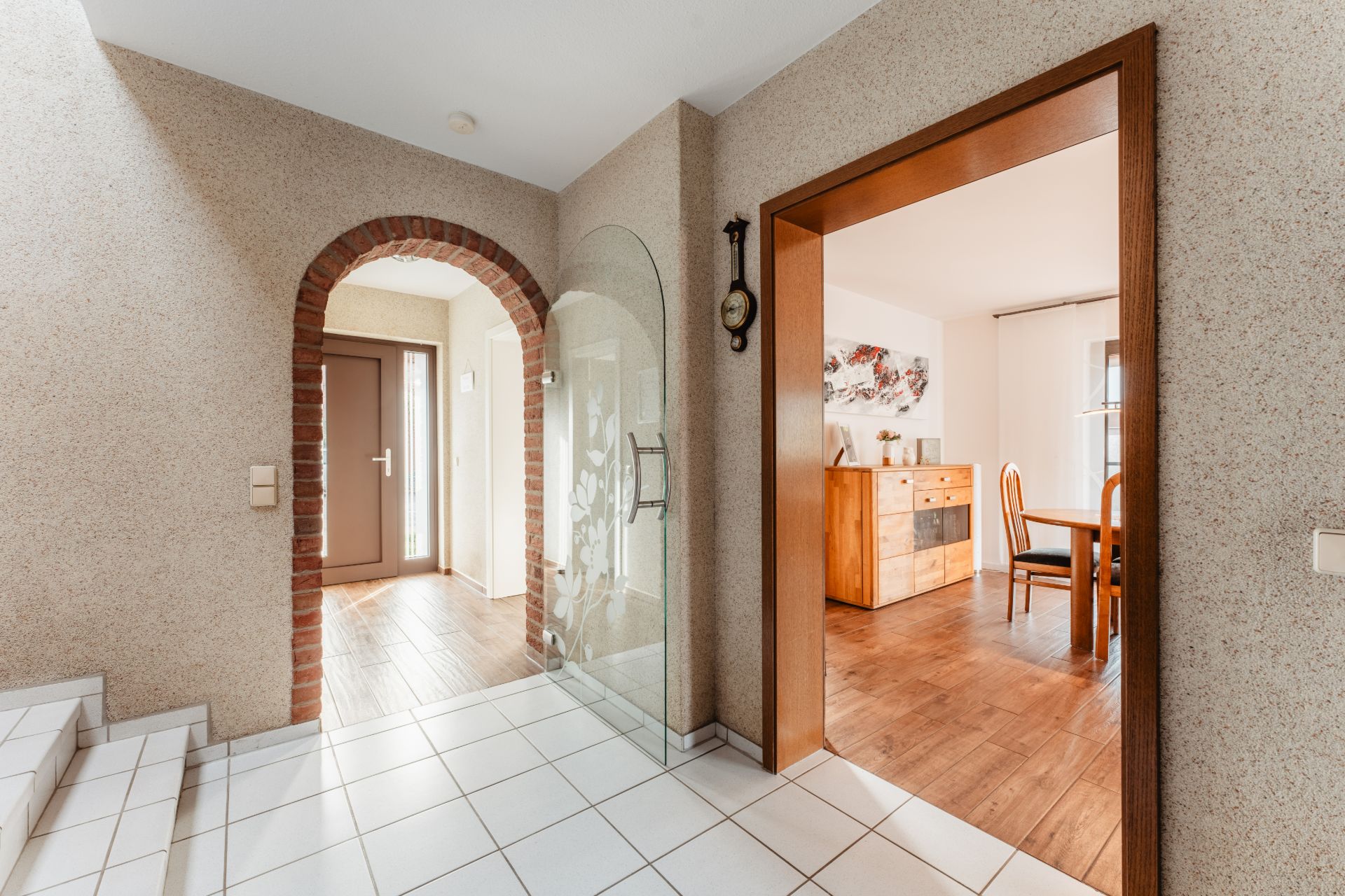 Heller Flur mit Glastür, Durchgangsbogen und Blick ins Esszimmer mit Holzboden.