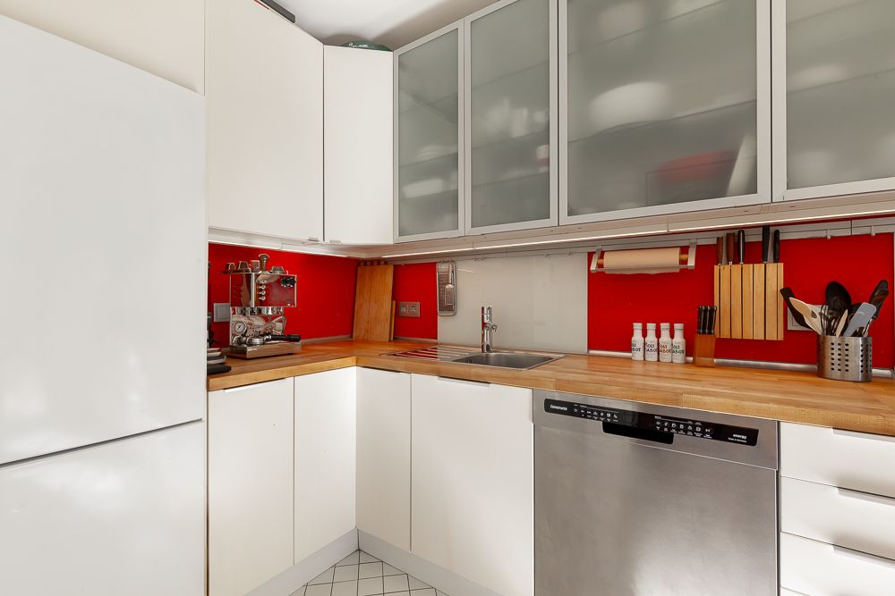 Moderne Küche mit weißen Schränken, Holzarbeitsplatte und roter Wandverkleidung.