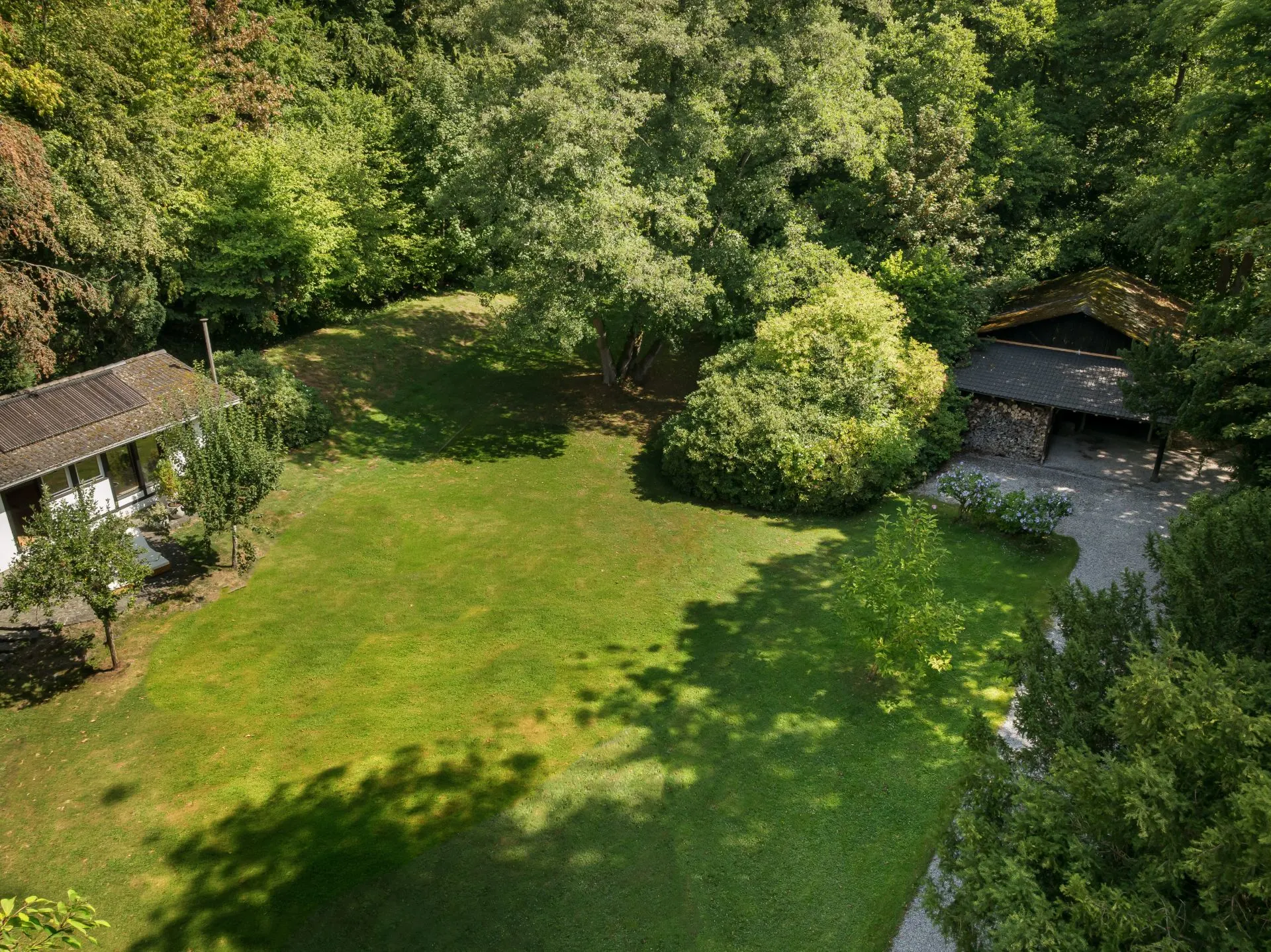 Großer grüner Garten mit Bäumen, Rasenfläche, Haus links und Schuppen rechts.
