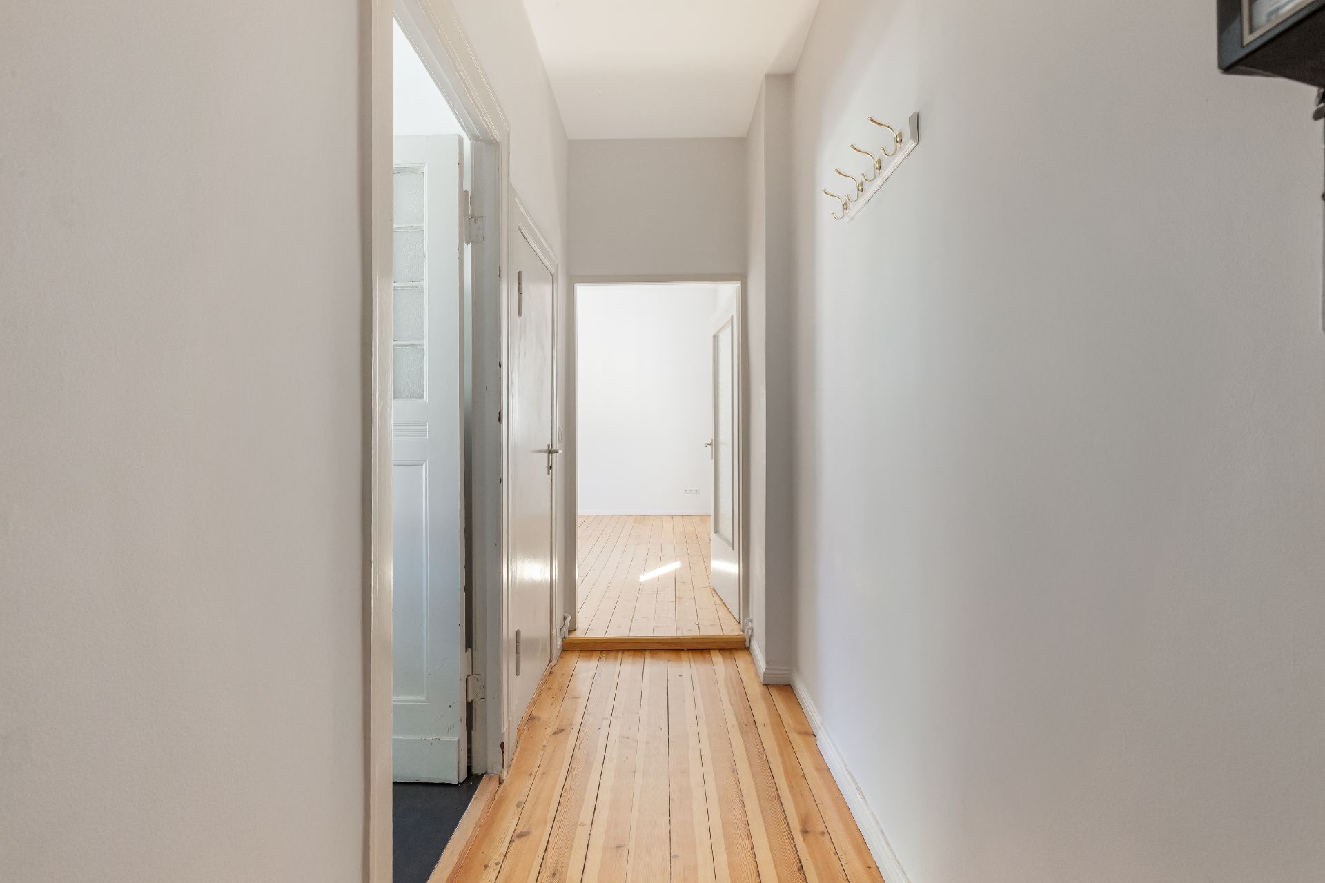 Heller Flur mit Holzboden, weißen Wänden und mehreren Türen.