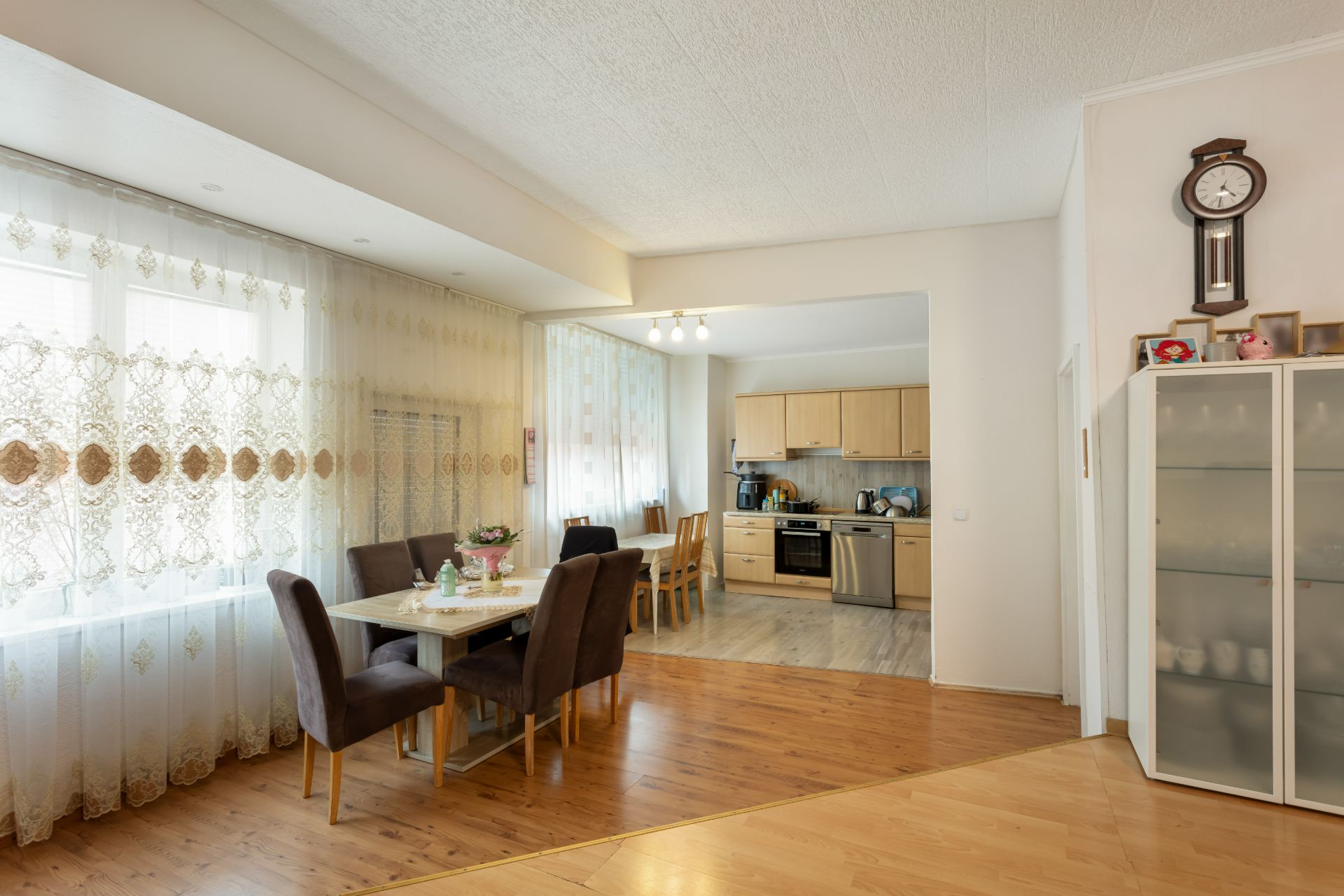 Esszimmer mit braunen Stühlen, großer Fensterfront und offener Blick in die helle Küche.