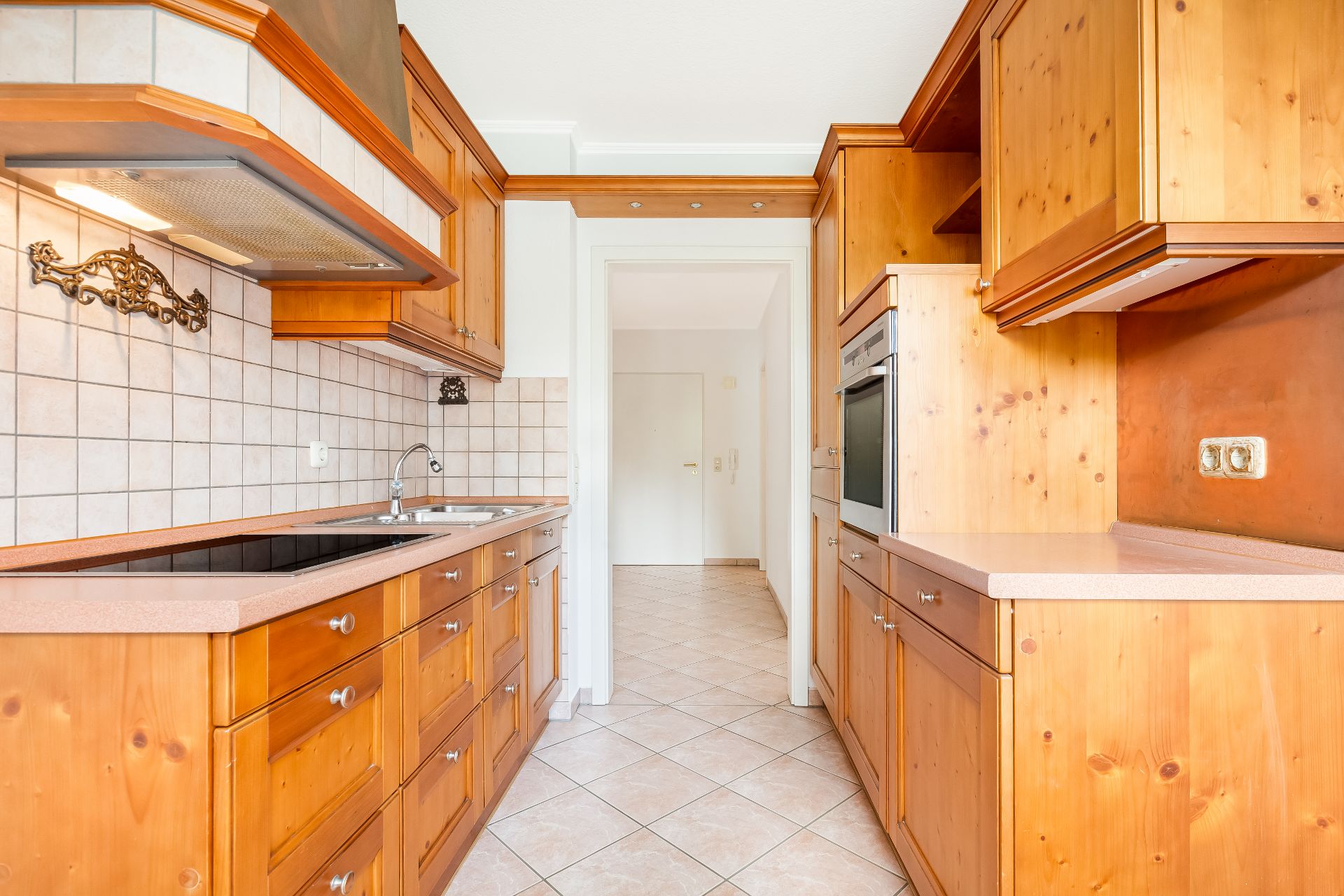 Helle Einbauküche mit Holzmöbeln, Herd, Spüle und Durchgang zum Flur.