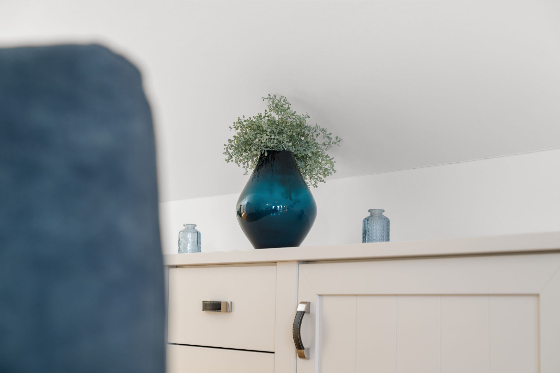 Blaue Vase mit Blume auf weißem Schrank, zwei kleine blaue Gefäße daneben.