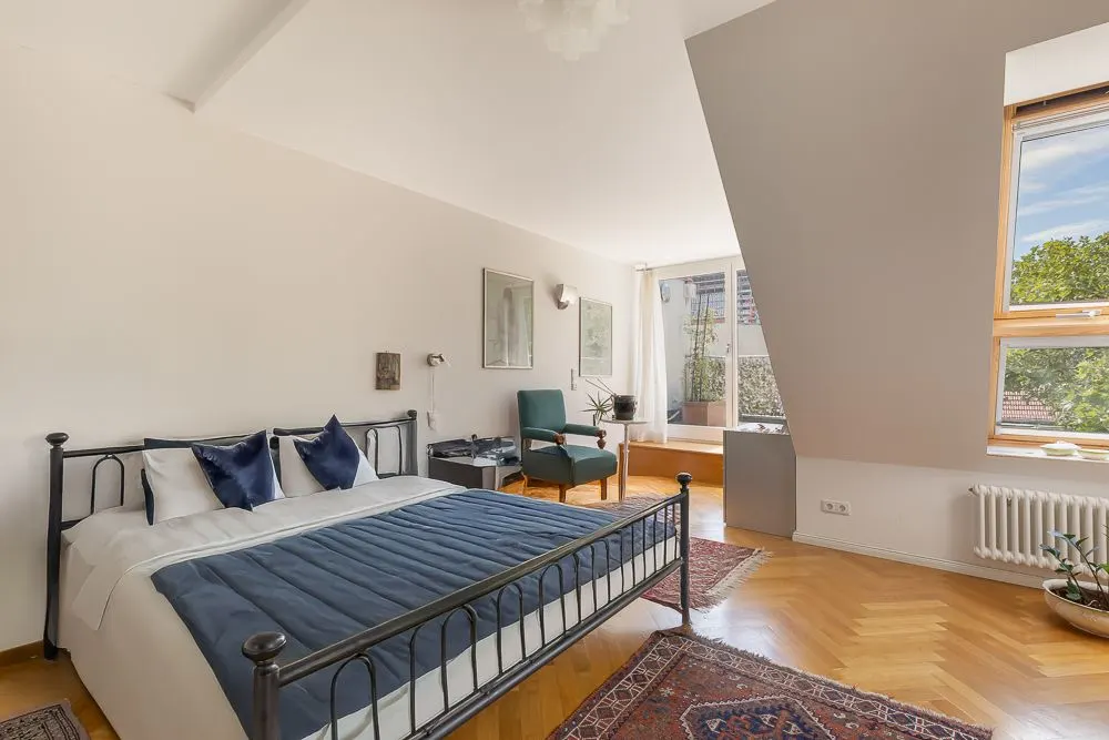 Helles Schlafzimmer mit Doppelbett, grünem Sessel und großen Fenstern mit Aussicht.