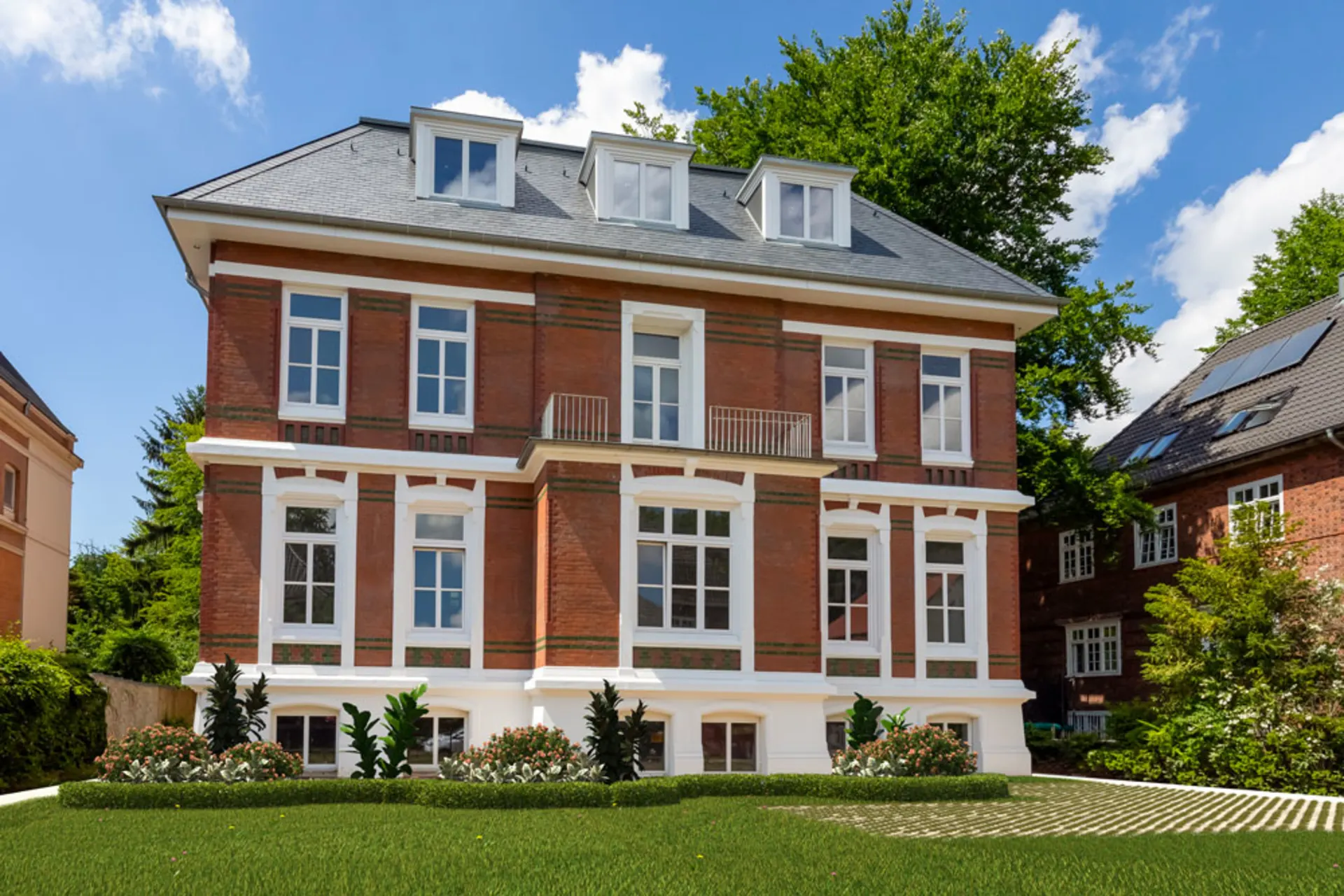 Großes, dreistöckiges Backsteinhaus mit weißen Fenstern und gepflegtem Vorgarten.