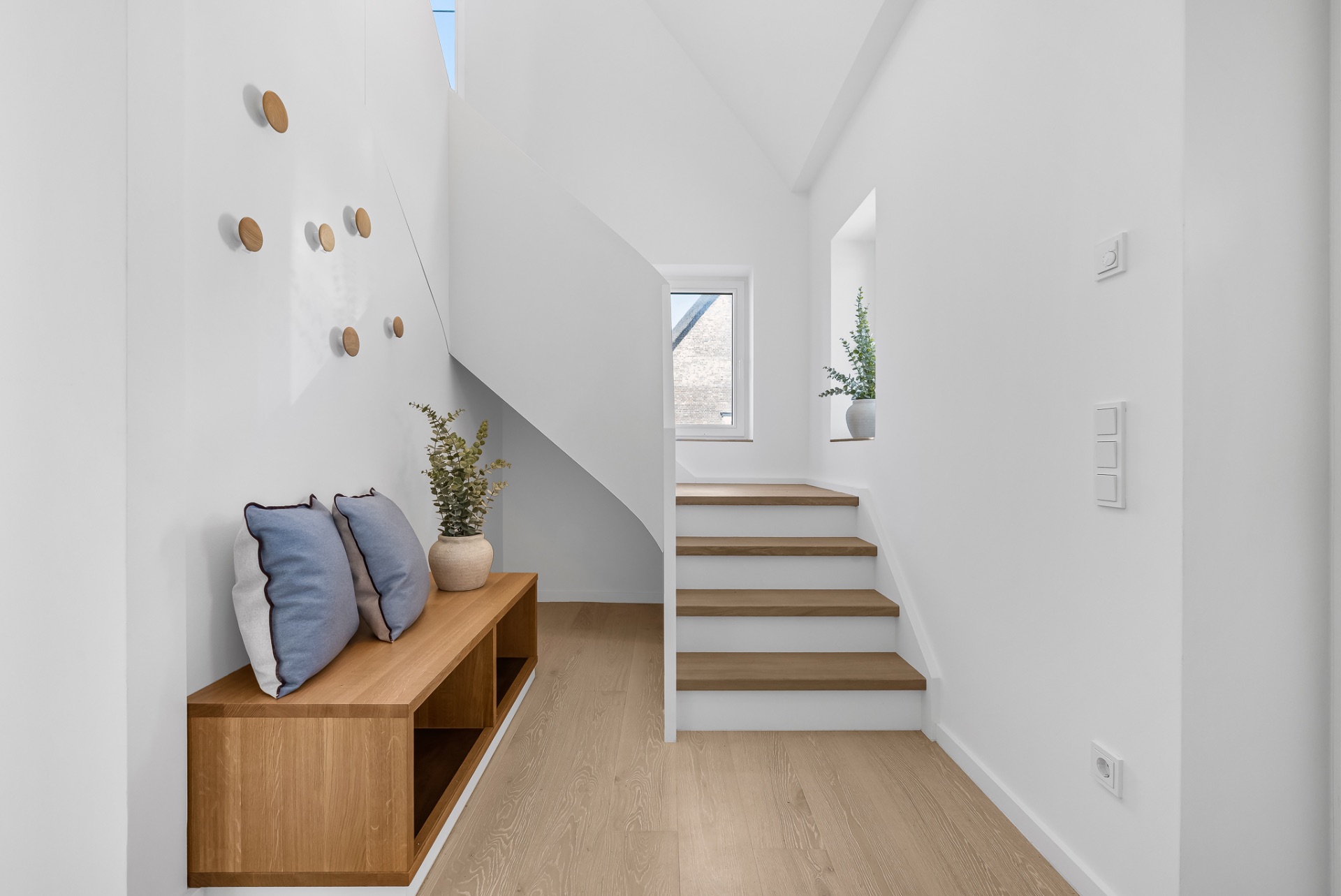 Heller Flur mit Holzbank, Kissen, Treppe, Pflanzen und Wanddekoration.