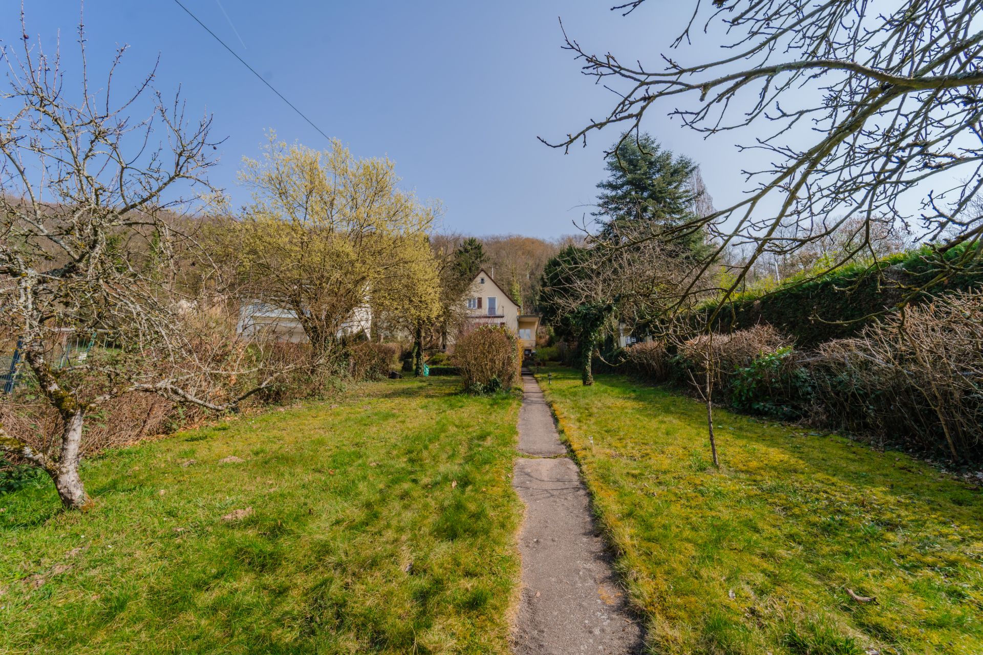 Garten mit Wiesenfläche, Bäumen und einem Weg zu einem Haus im Hintergrund.
