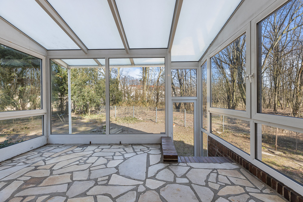 Heller Wintergarten mit großen Fenstern und Steinboden, Blick in den Garten.