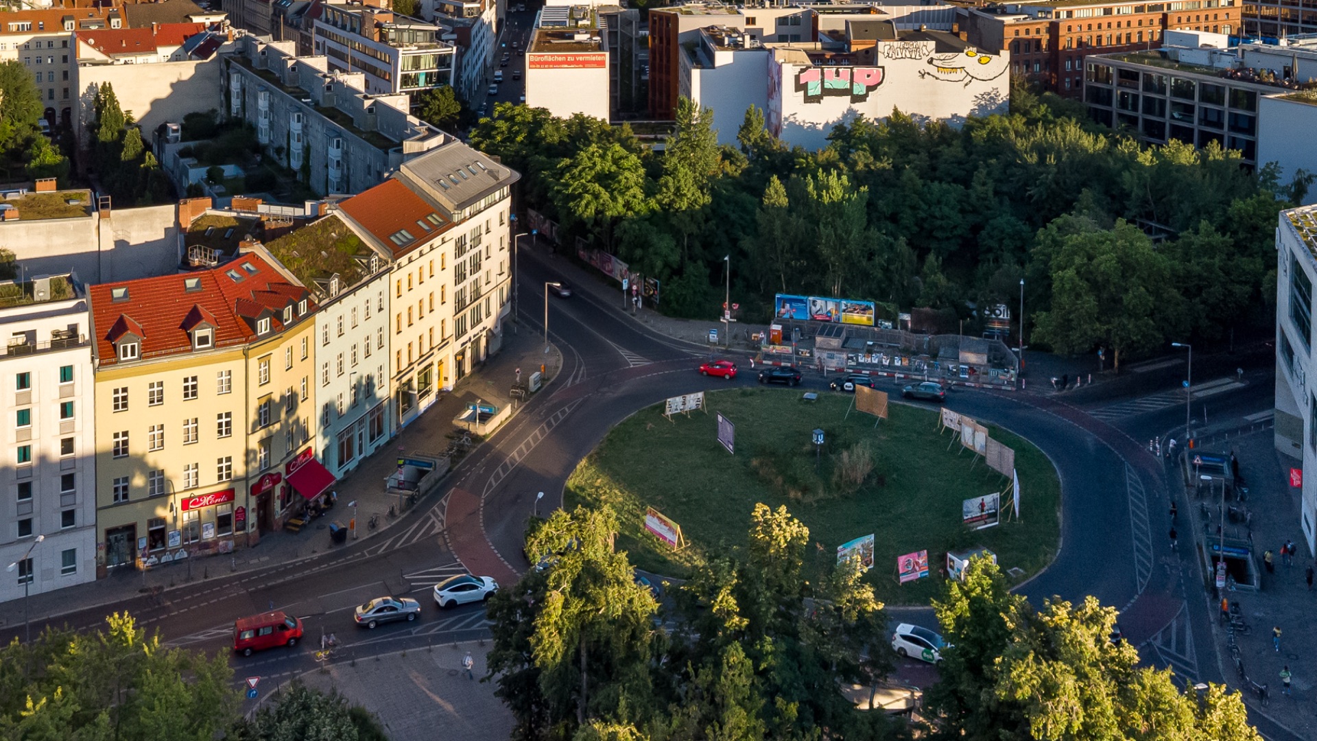 Kreisverkehr mit grüner Insel, umliegenden Wohnhäusern und Bäumen im Hintergrund.