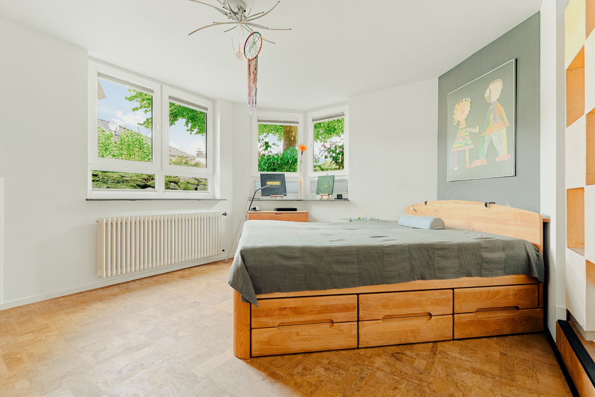 Helles Schlafzimmer mit großem Holzbett, Schreibtisch und mehreren Fenstern.