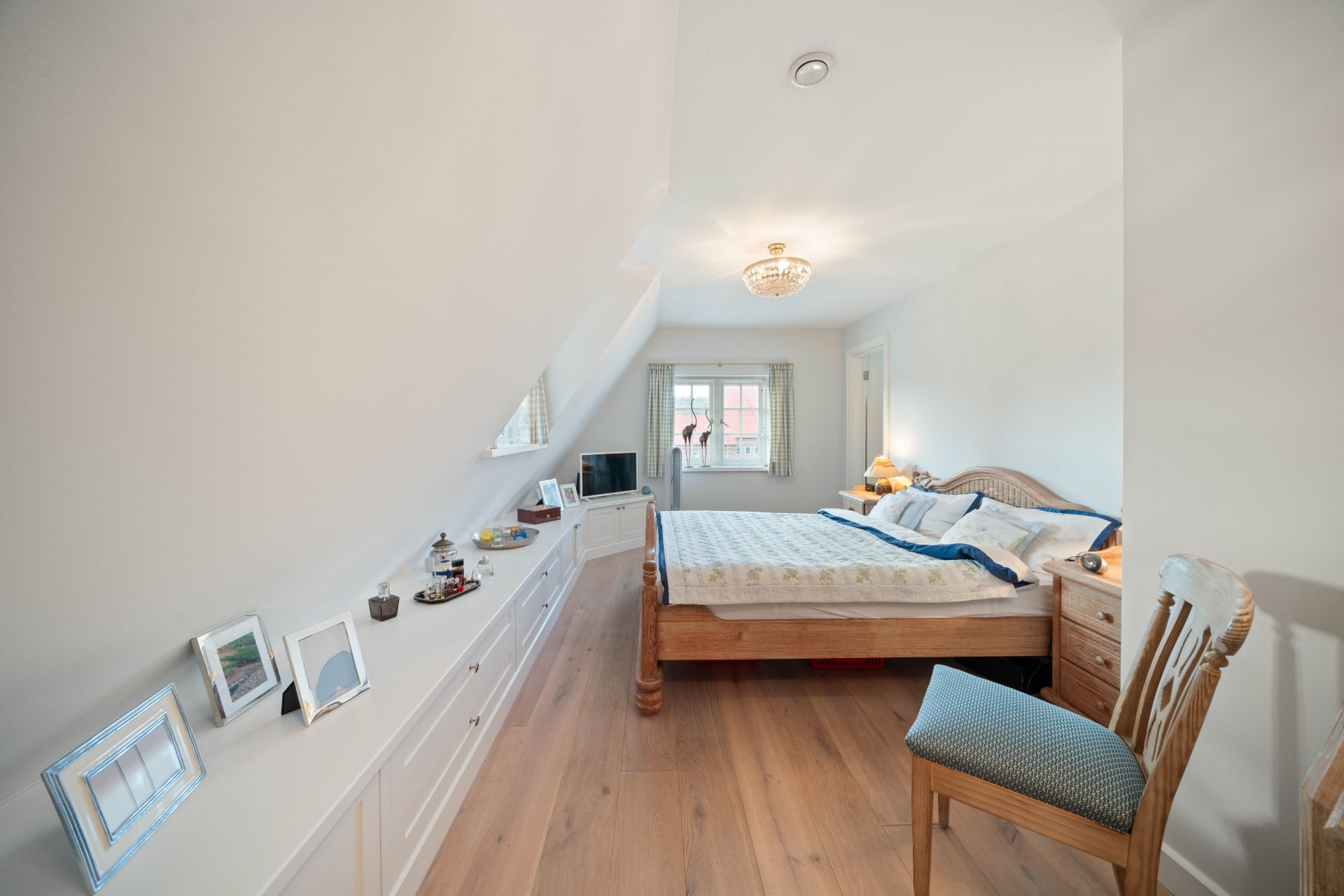 Helles Schlafzimmer mit Holzboden, Doppelbett, Kommode, Stuhl und Fenstern.