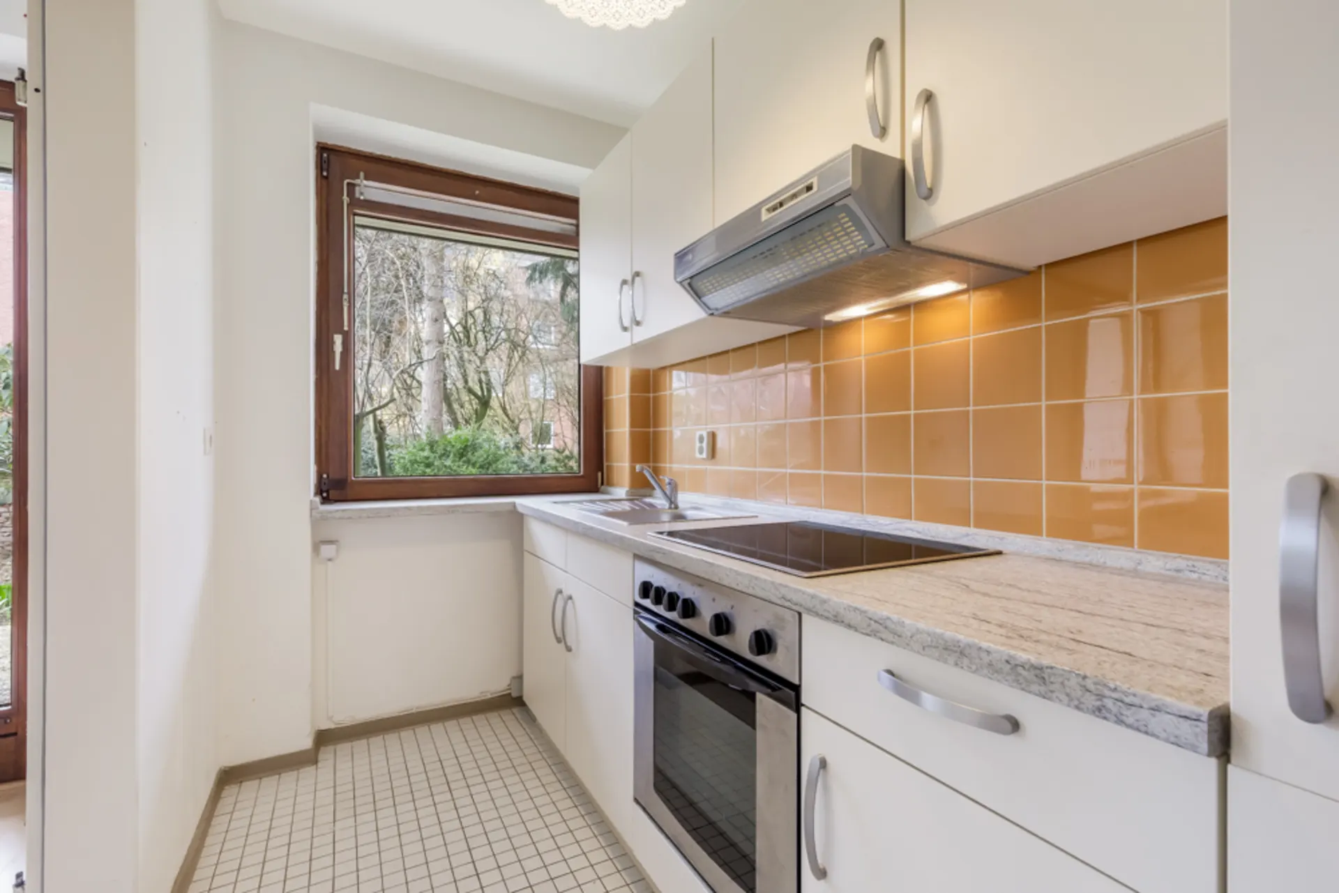 Helle Küche mit großem Fenster, Elektroherd, Backofen und gelben Fliesen an der Wand.
