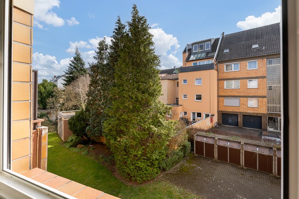 Blick aus dem Fenster auf einen Garten mit Bäumen und angrenzenden Garagen.
