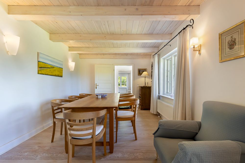 Esszimmer mit Holztisch, Stühlen, Sessel und Fenster, helle Wände und Decke aus Holz.