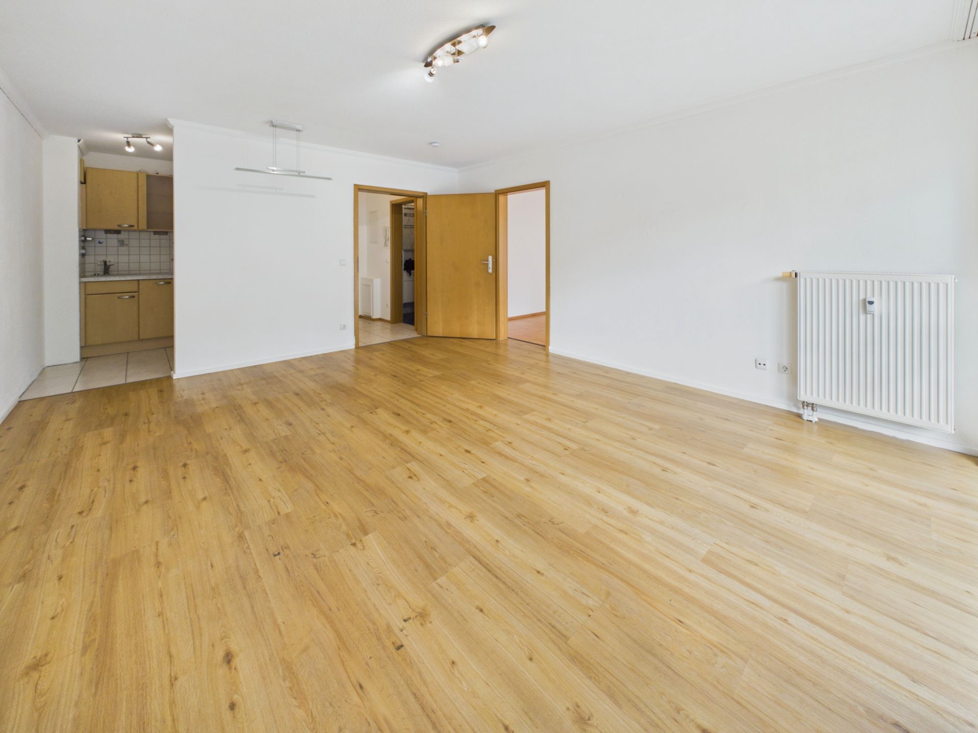 Helles Wohnzimmer mit Holzfußboden, offener Küche und weißen Wänden.