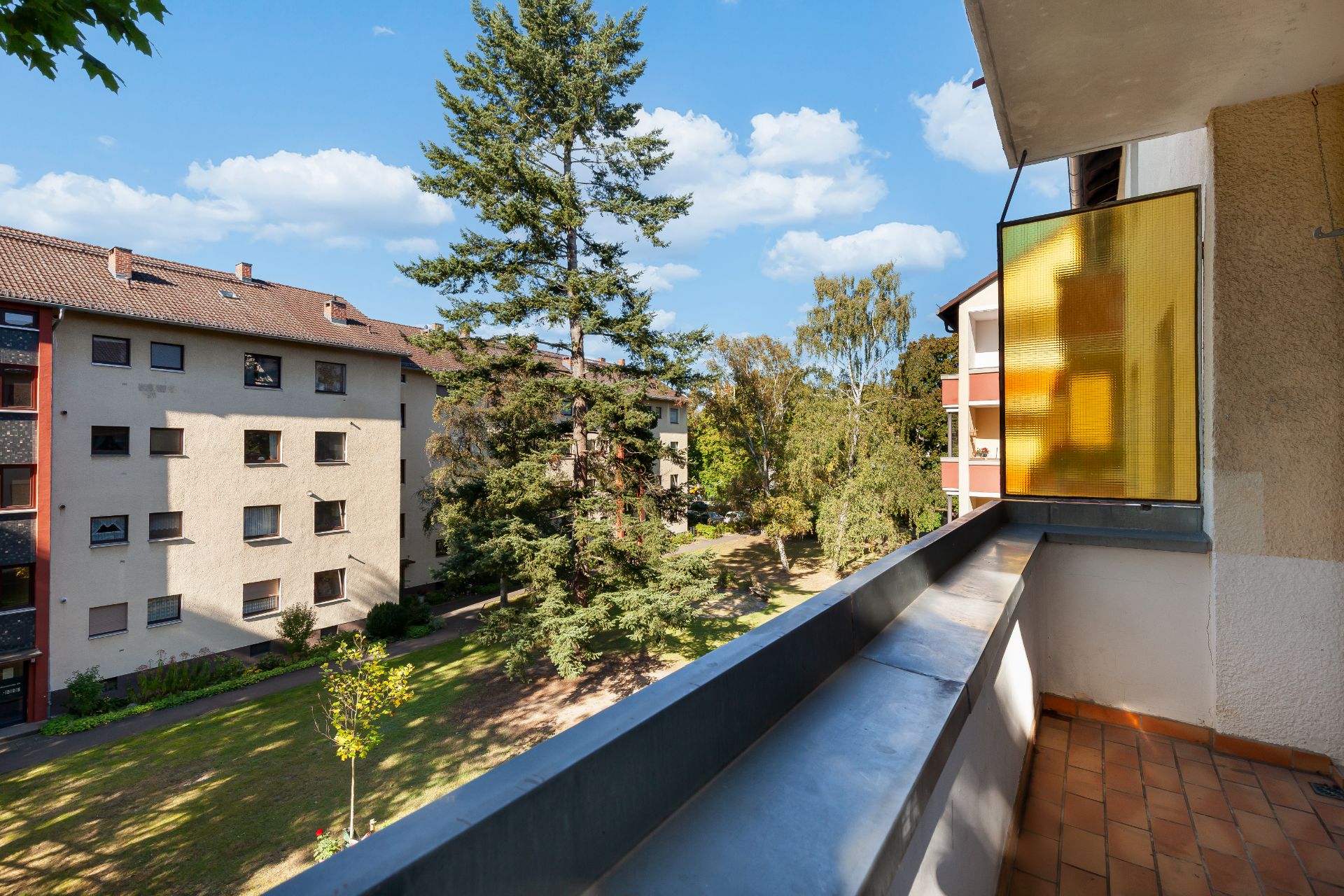 Blick von einem Balkon auf einen begrünten Innenhof mit Wohngebäuden und Bäumen.