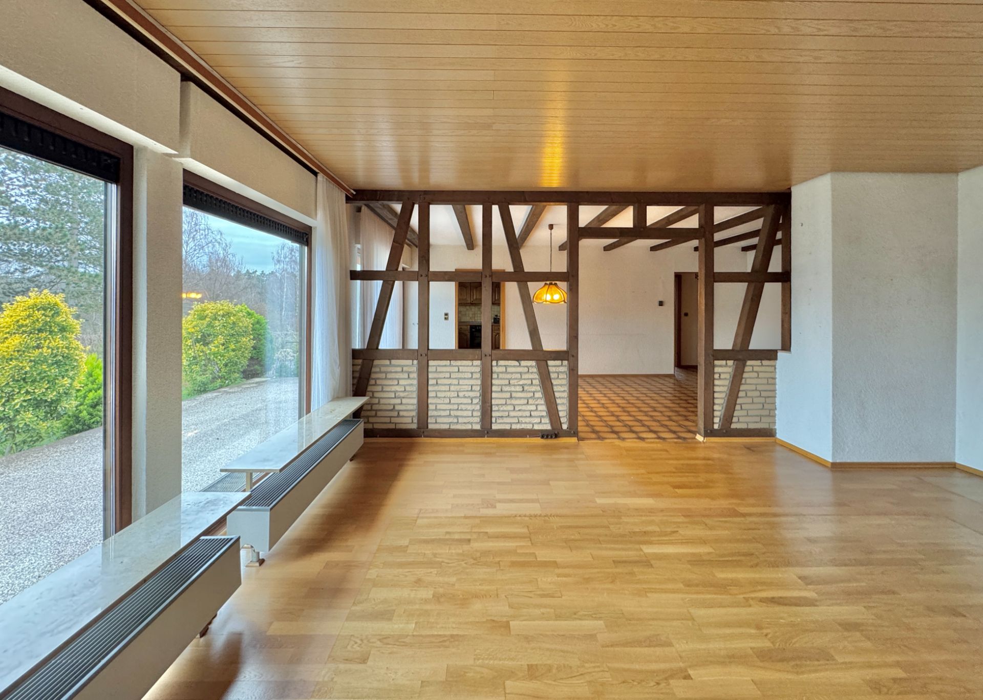 Heller Raum mit Holzfußboden, großen Fenstern und einer Fachwerkwand zur angrenzenden Fläche.