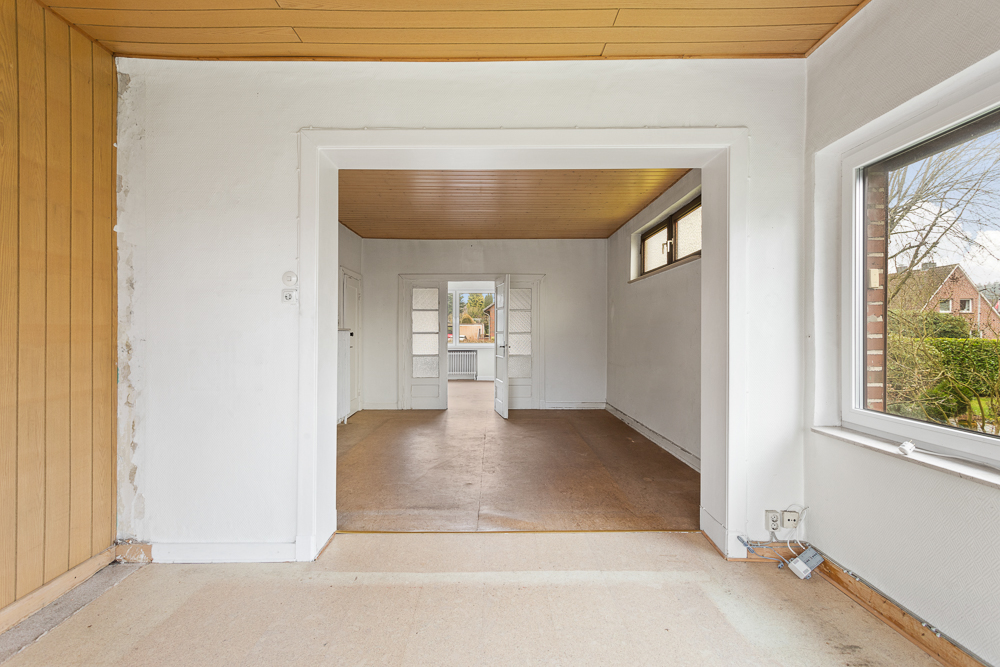 Leerer Raum mit Holzdecke, weißen Wänden und einem Fenster mit Blick nach draußen.