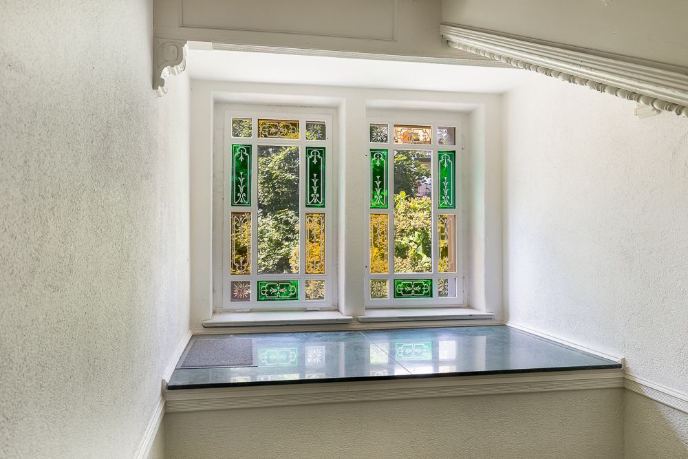 Fenster mit buntem Glas und grünen Verzierungen in einem hellen Flur.