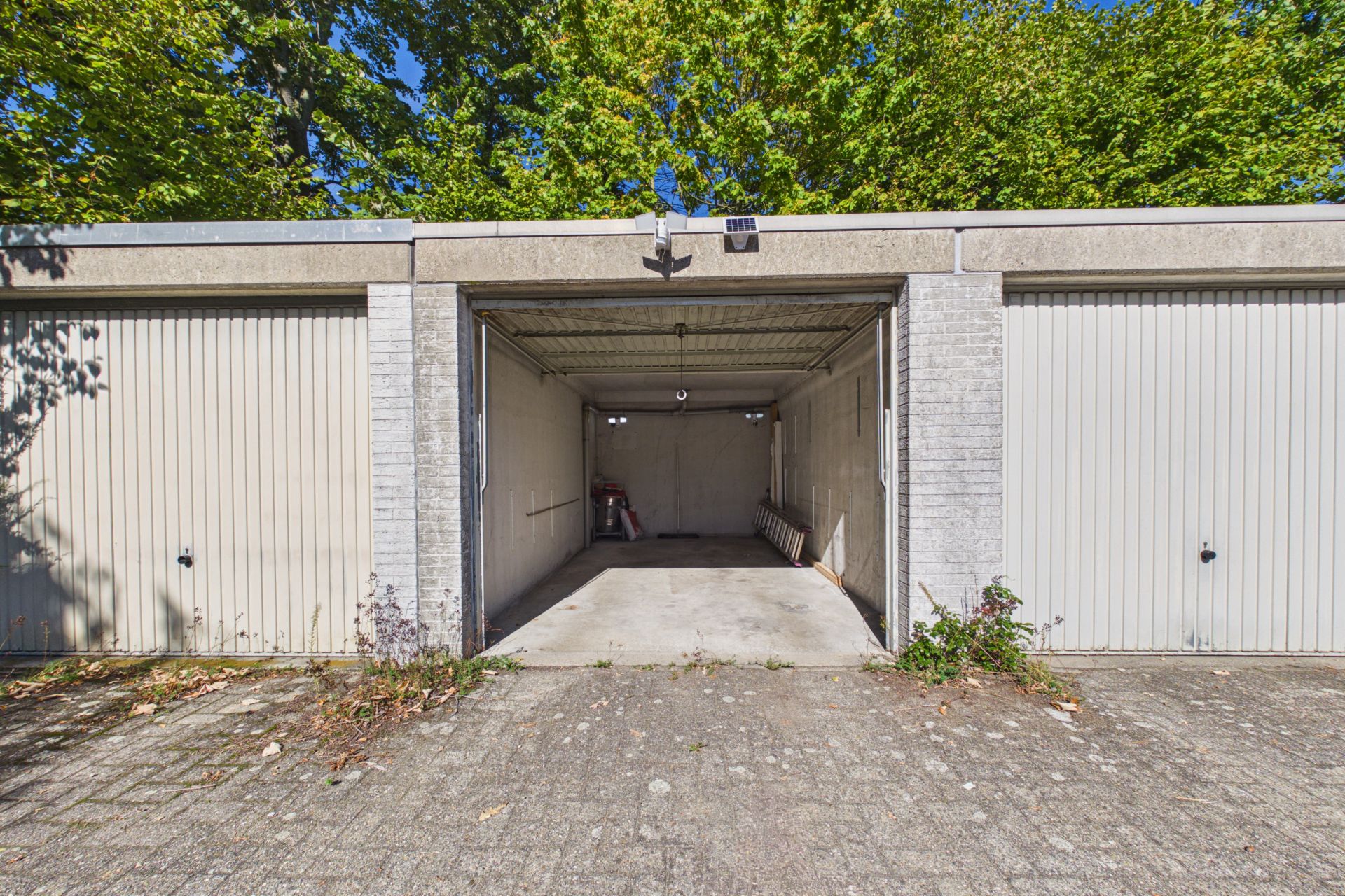 Offene Einzelgarage mit Betonboden und sichtbarem Innenraum, daneben geschlossene Garagentore.